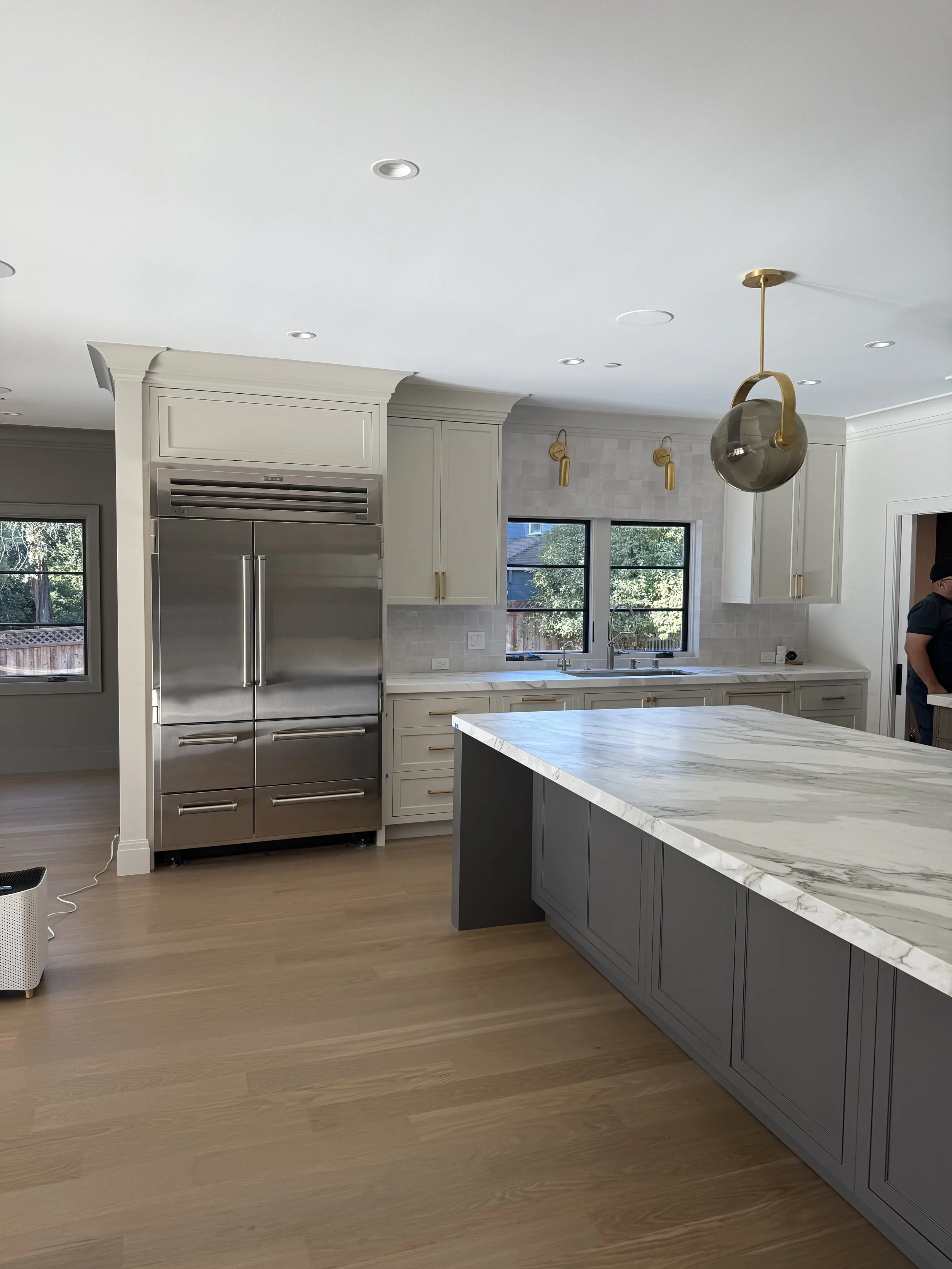 Kitchen with white cabinetry, a large veined stone island, and pendant lights.