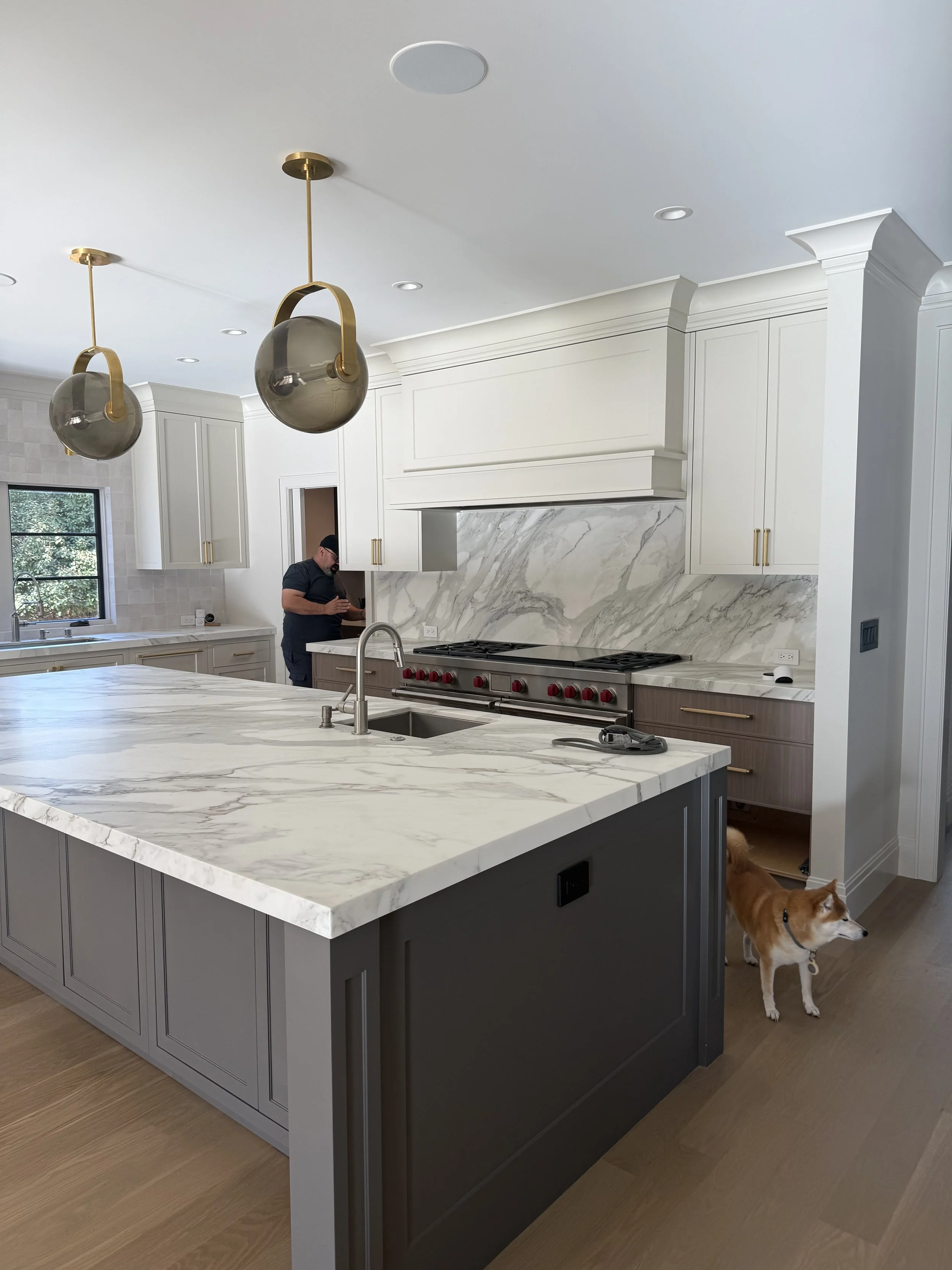 Kitchen with white cabinets, a large island, and a veined stone backsplash.