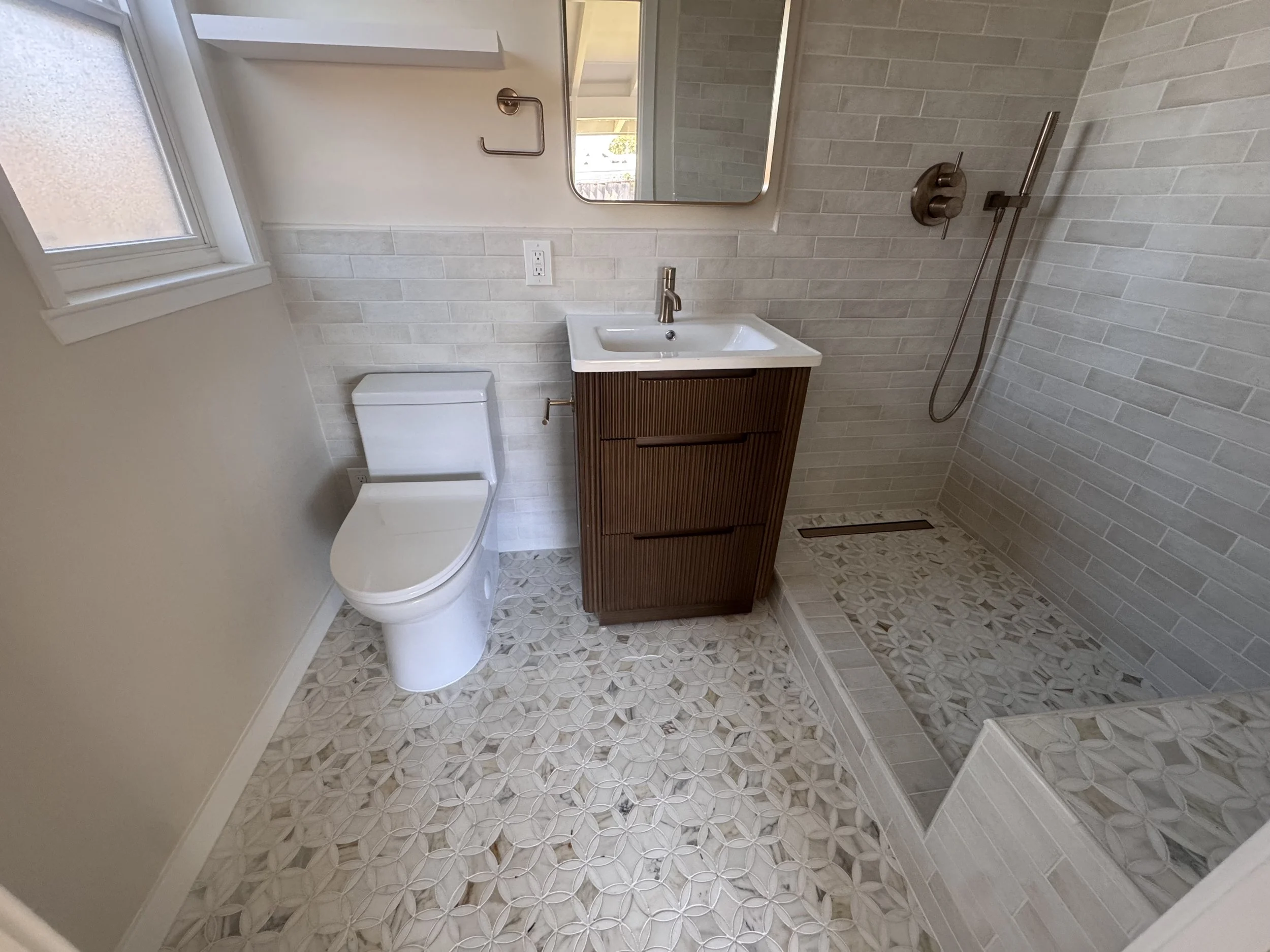 Bathroom renovation with a wood vanity, patterned tile, and a walk-in shower.