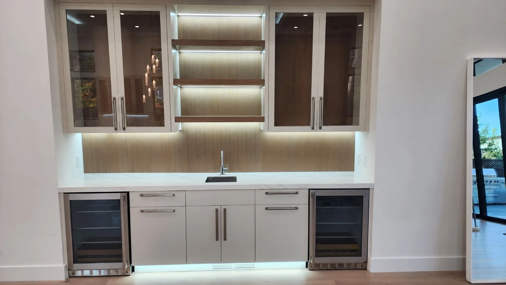 Custom home bar with illuminated shelving, a stone countertop, sink, and built-in beverage coolers.