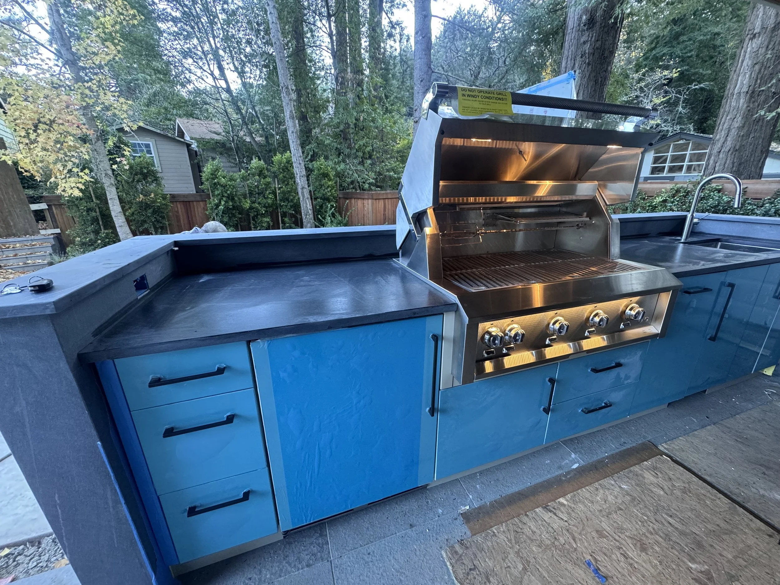 Outdoor kitchen with blue cabinetry, a stainless steel grill, and a sink.