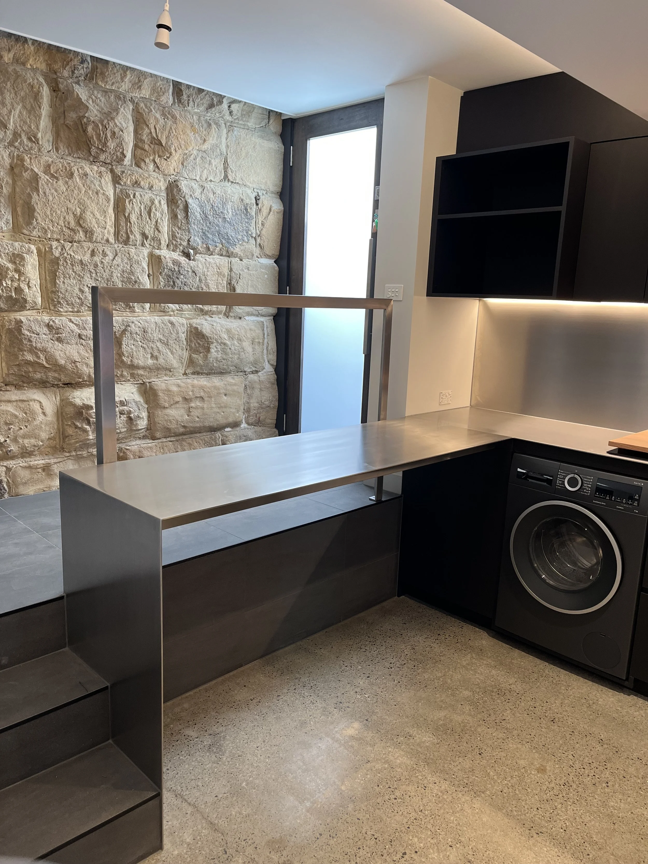 5mm stainless steel plate benchtops with a waterfall end, featuring a brushed satin  finish, in a laundry/kitchenette installed at a private residence at North Hobart.