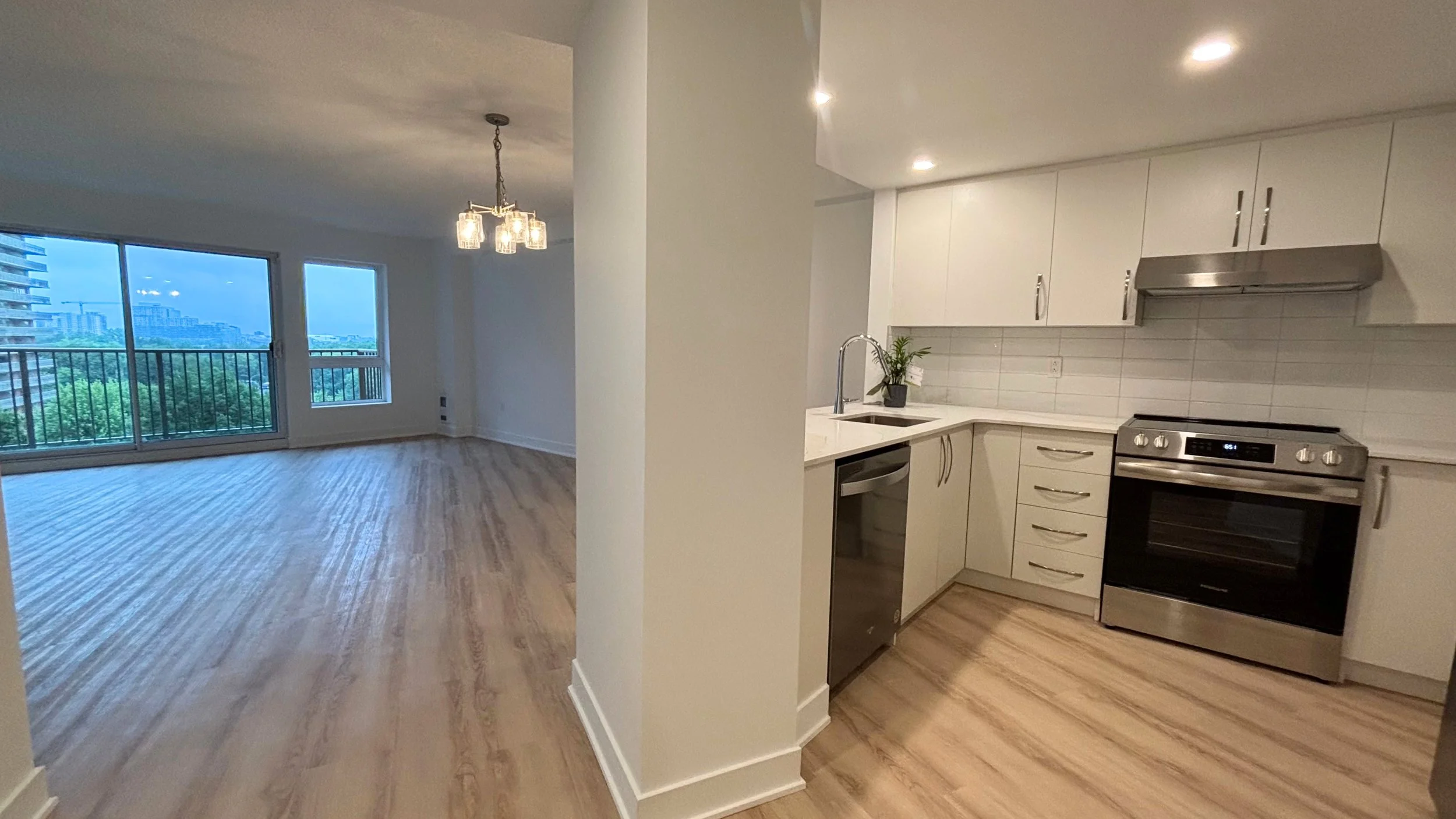 Cuisine ouverte aux armoires blanches fraîchement repeinte dans un condo du secteur Chomedey à Laval, vue sur les tours voisines