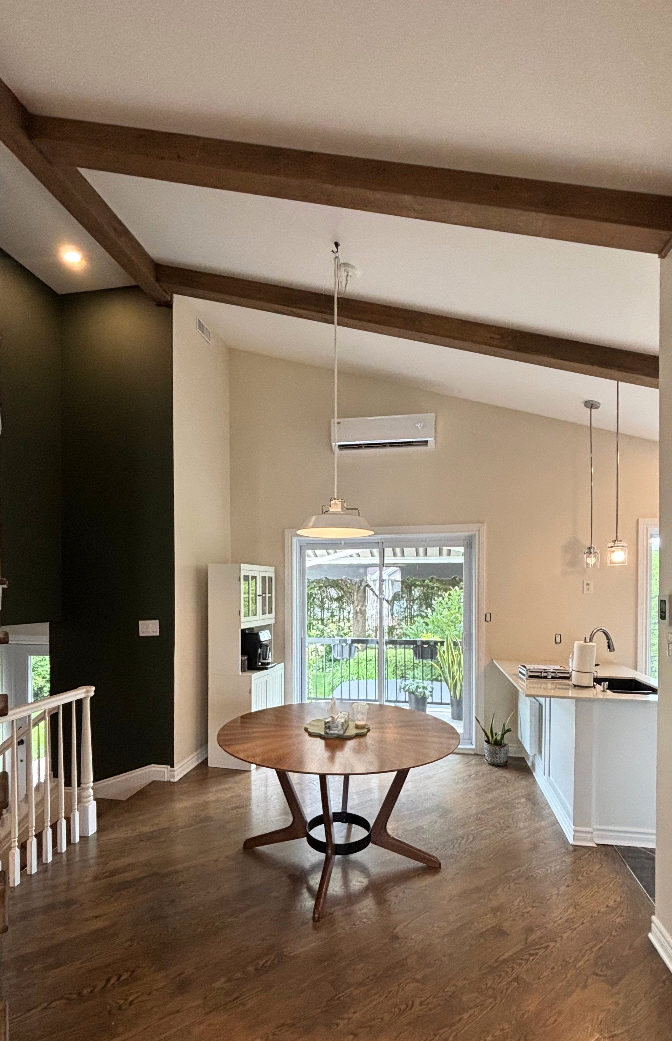 Salle à manger à aire ouverte fraîchement repeinte avec mur d'accent vert foncé, murs crème et poutres apparentes, maison à Terrebonne sur la Rive-Nord