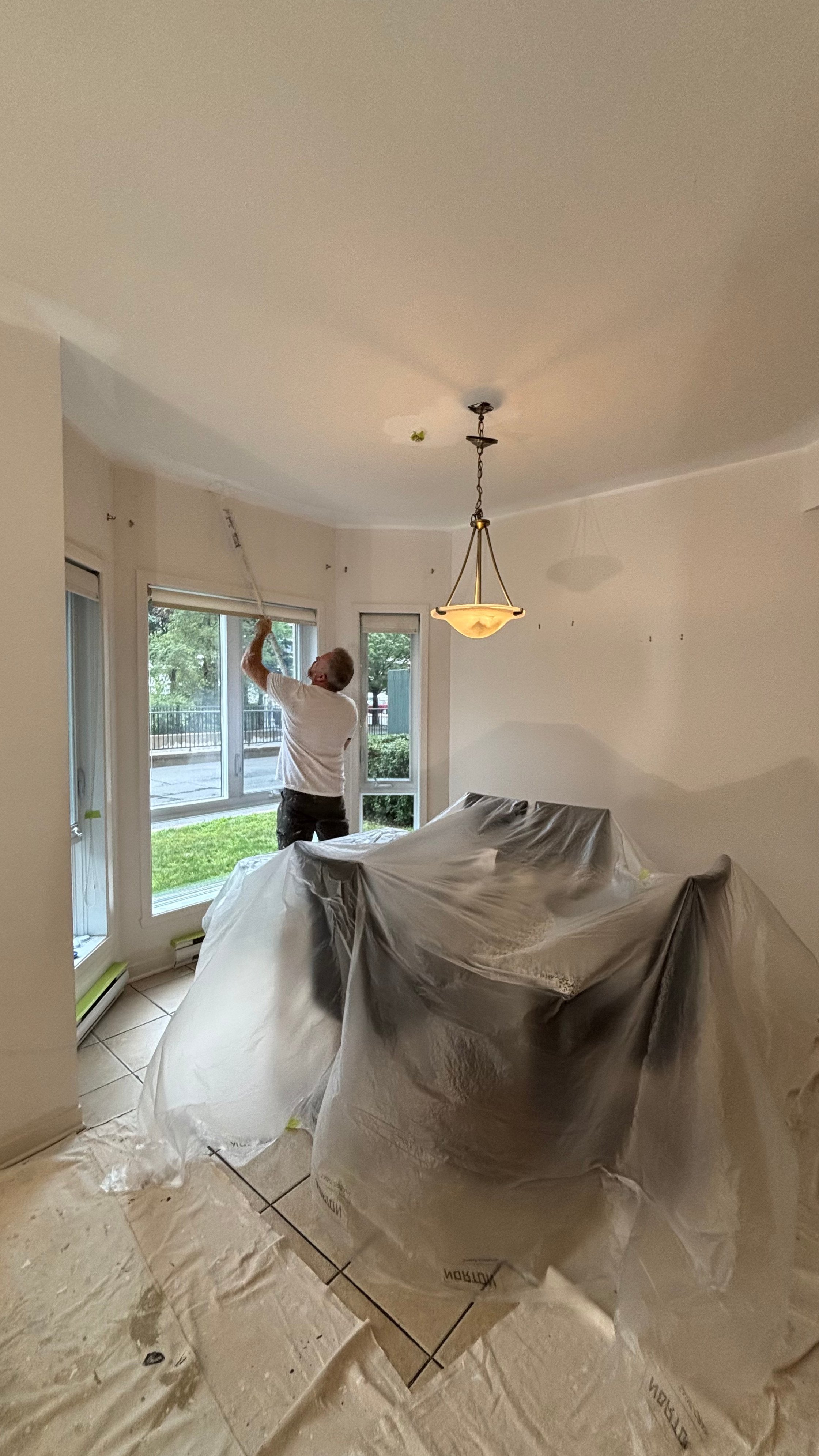 Patrick Jacob, un des copropriétaires de MP Peinture, roulant un plafond dans un condo à Laval, meubles protégés de plastique