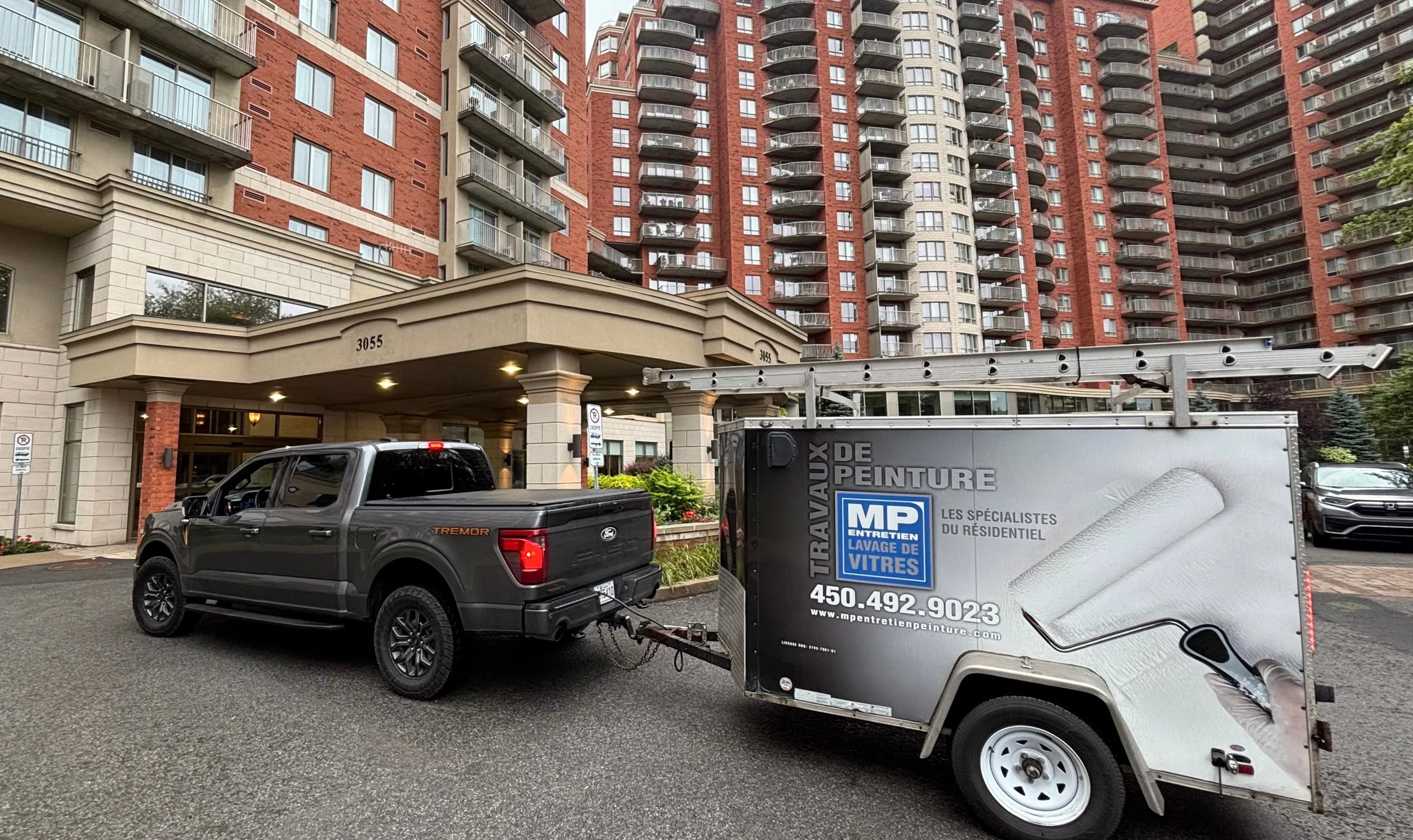 Camion et remorque lettrés de MP Entretien Peinture devant une tour à condos en brique rouge du secteur Chomedey à Laval