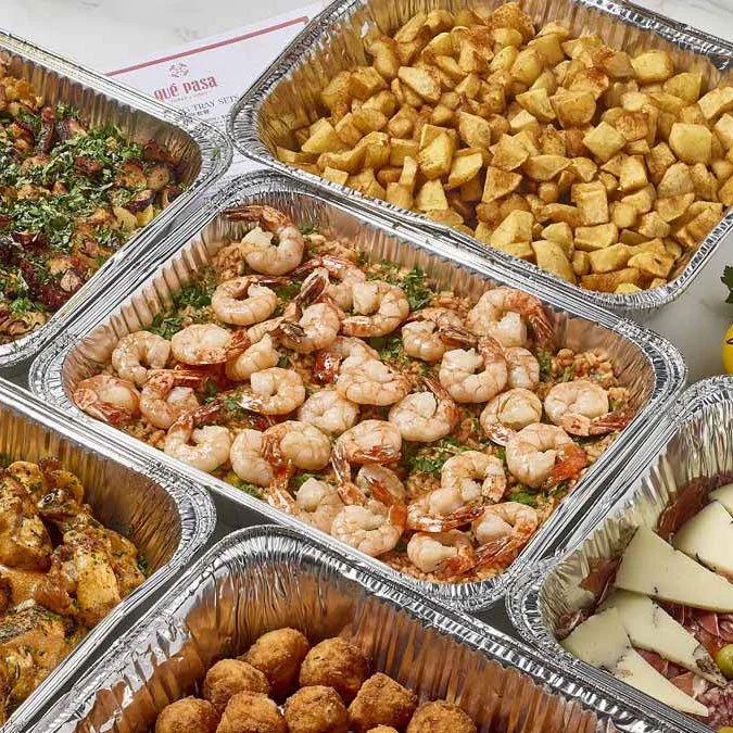 Aluminum trays filled with various dishes including cooked shrimp, diced potatoes, and other appetizers at a buffet.