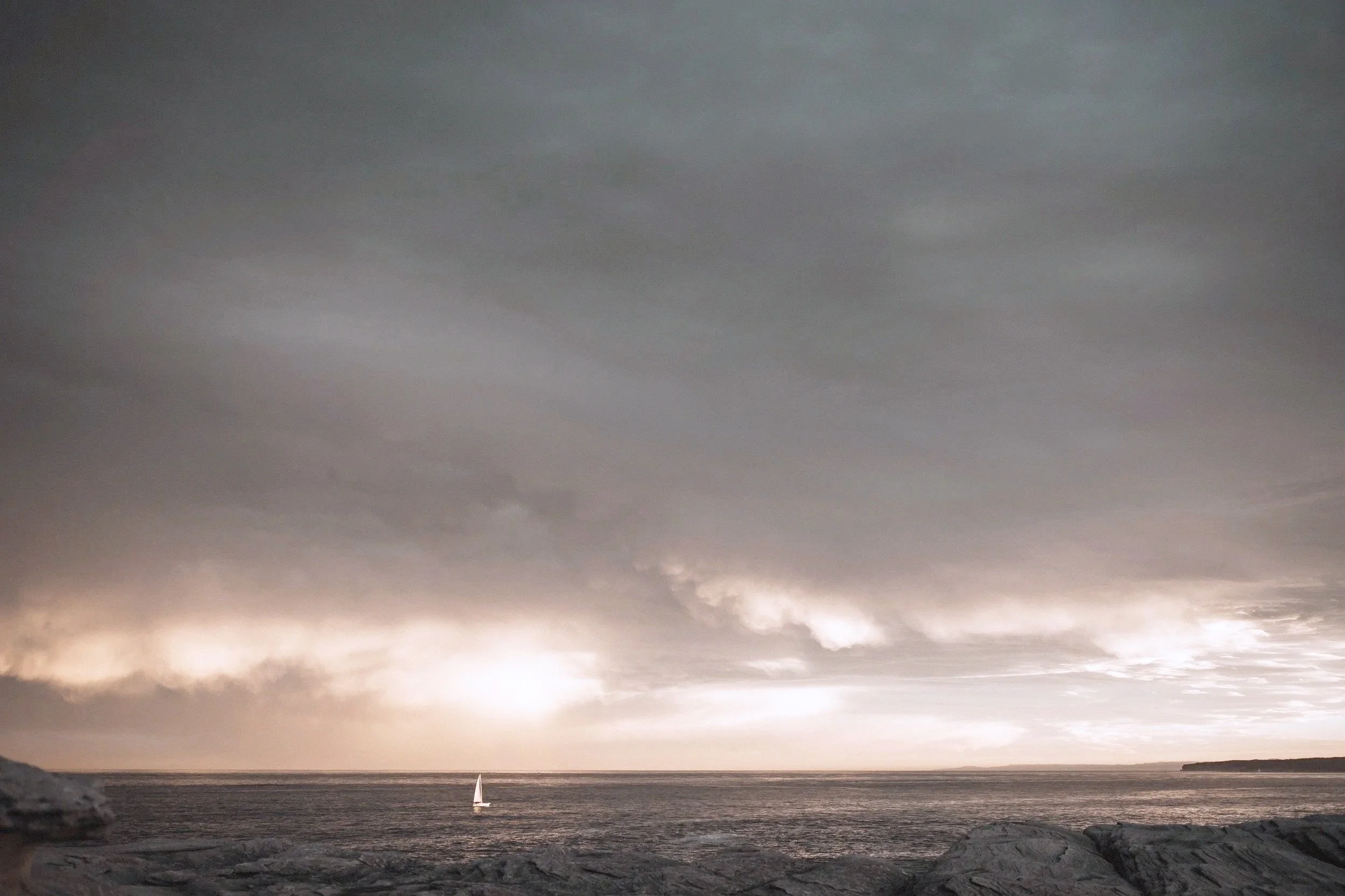 A sailboat on the ocean during overcast weather with dark clouds and a cloudy sky.