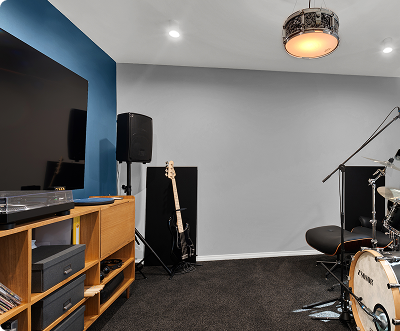 Music rehearsal room with a drum set, microphone stand, guitar, speaker, and storage unit.