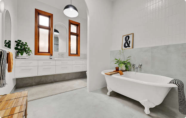 Modern bathroom with white walls and a clawfoot bathtub, green plants, and a wooden framed mirror.