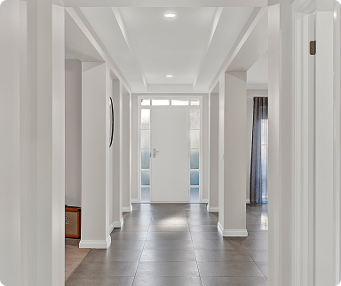 Bright, modern hallway with white walls, gray tile flooring, and a front door with glass panels, leading outside.
