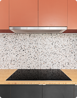 Kitchen countertop with built-in black stovetop, speckled backsplash, pink upper cabinets, and gray lower cabinets.