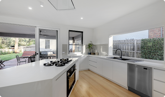 Modern kitchen with white cabinets, a large window facing the backyard, and a built-in stove on the island.