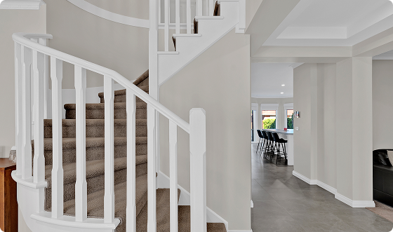 Interior view of a modern home with a staircase, white walls, and an open kitchen area with bar stools.