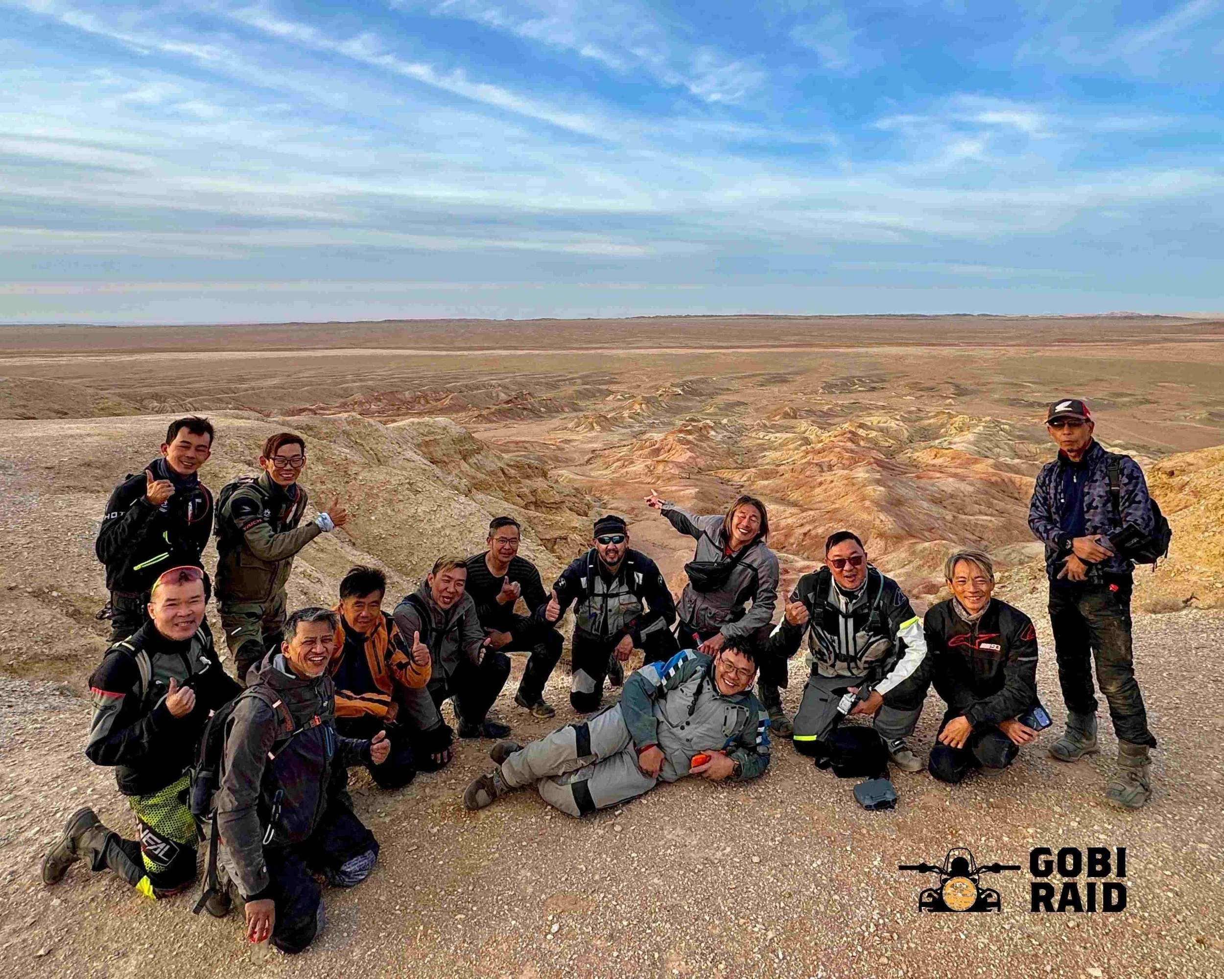 Group of people hiking at a desert landscape with colorful rock formations, blue sky, and eclouds. They are wearing outdoor gear and smiling.