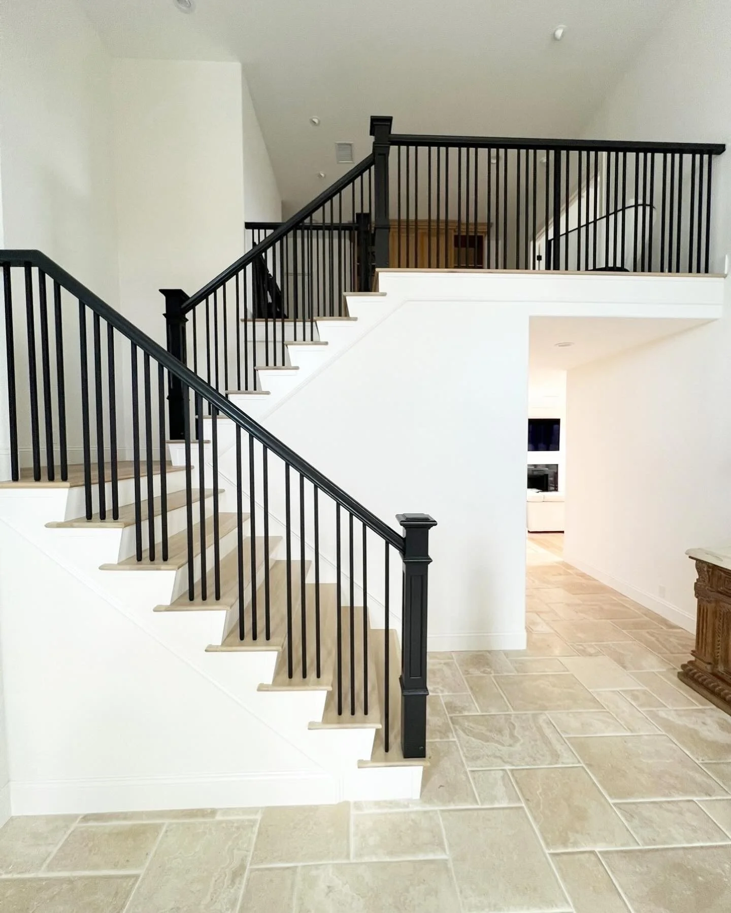 Interior view of a staircase with beige steps, black railing, and white walls, leading to an upper level in a modern home.