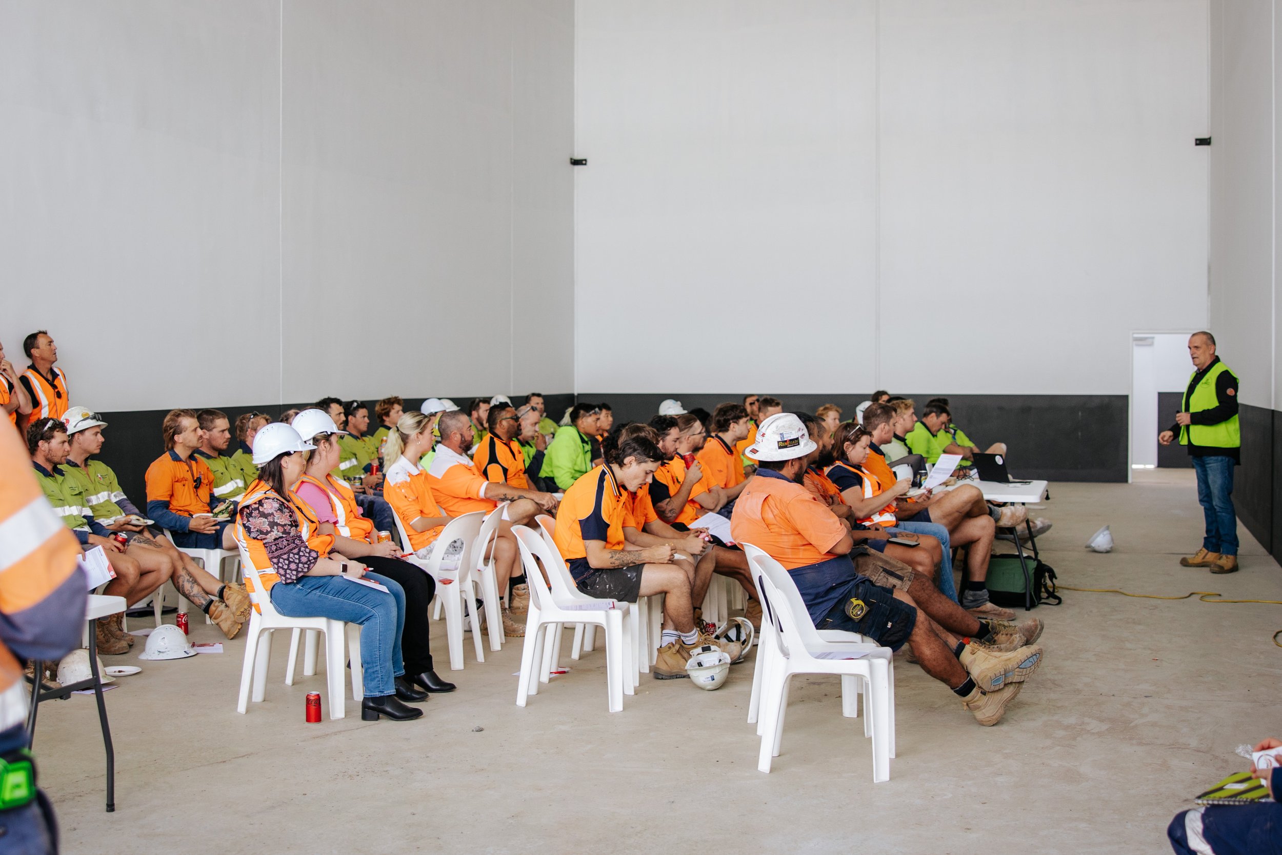 Construction workers in safety vests and helmets attending a training session indoors.