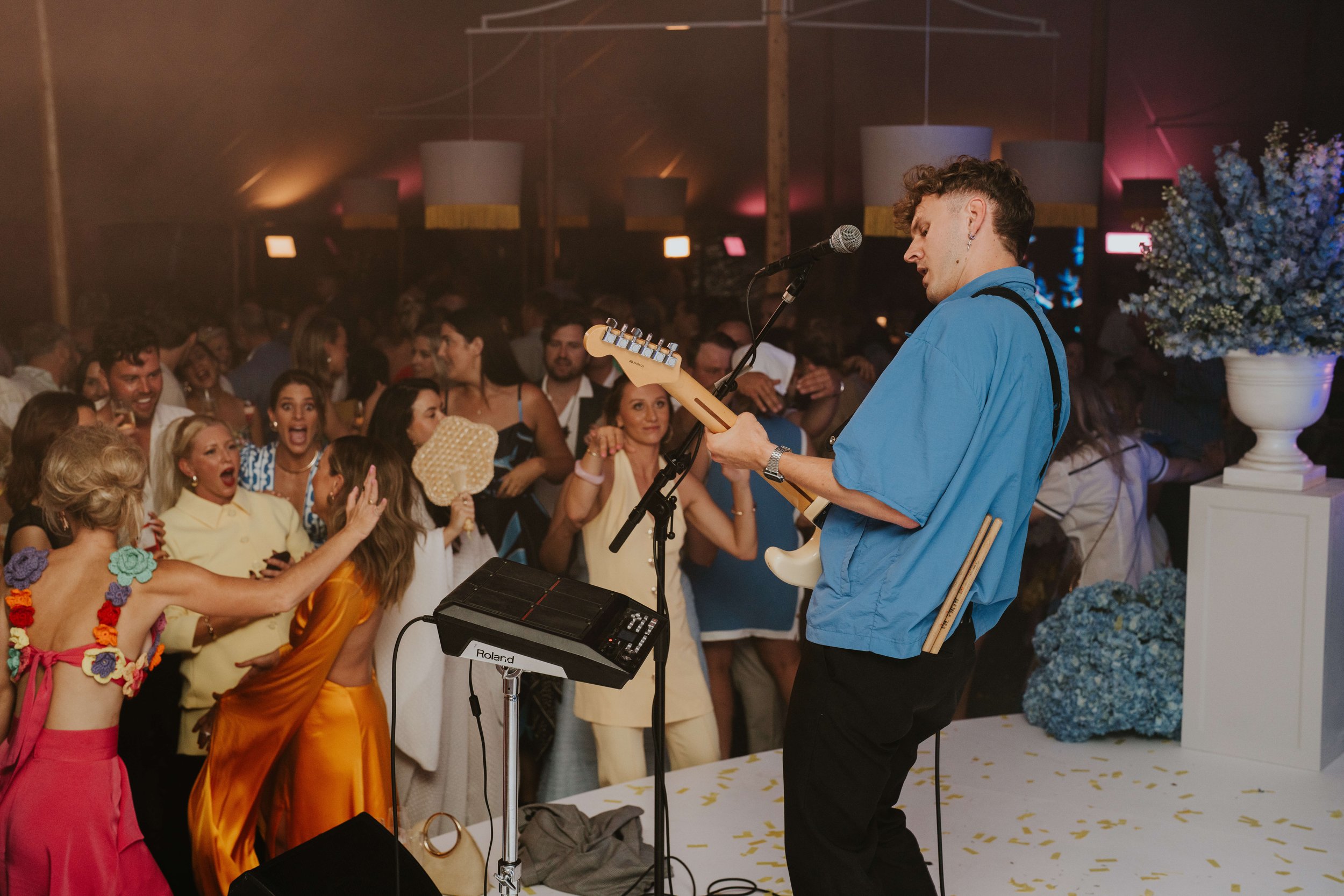 Band performing on stage at a lively party with a crowd dancing and cheering, surrounded by colorful decorations.