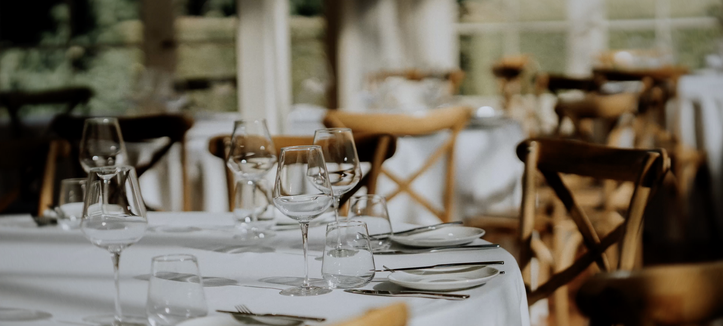 Elegant restaurant table setting with wine glasses, plates, cutlery, and wooden chairs.
