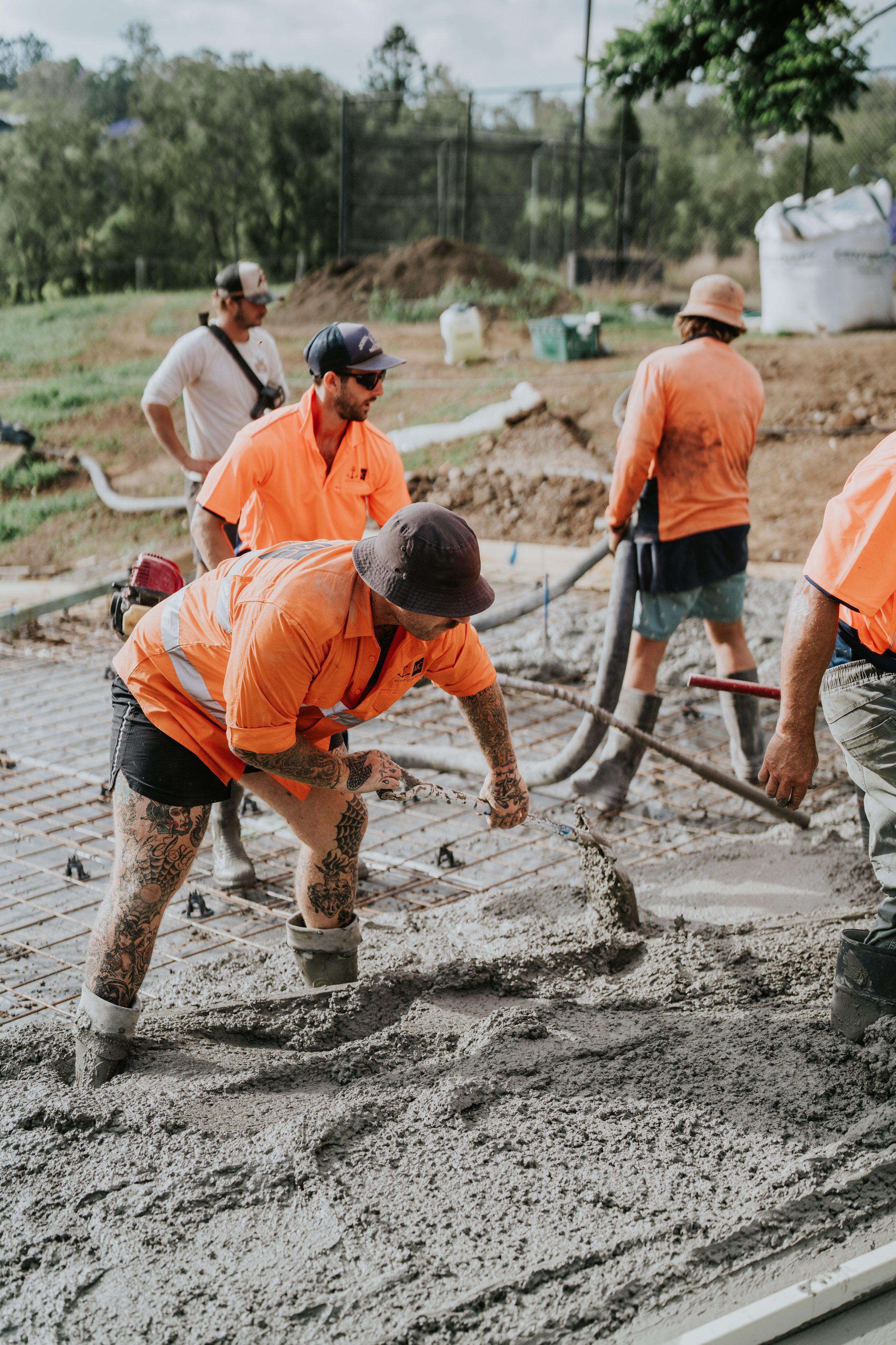 Construction workers pouring and smoothing wet concrete on a rebar foundation outdoors.