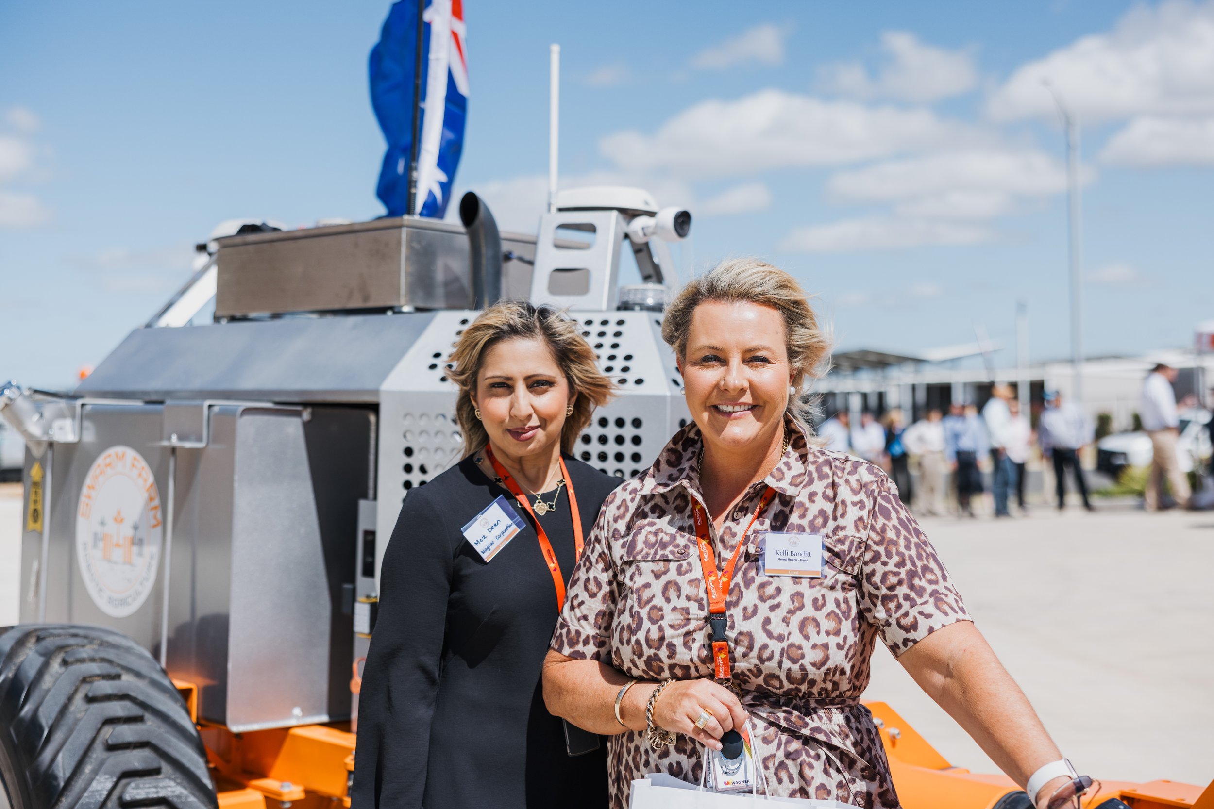 Two women standing in front of a high-tech vehicle with an Australian flag, wearing identification badges and lanyards.