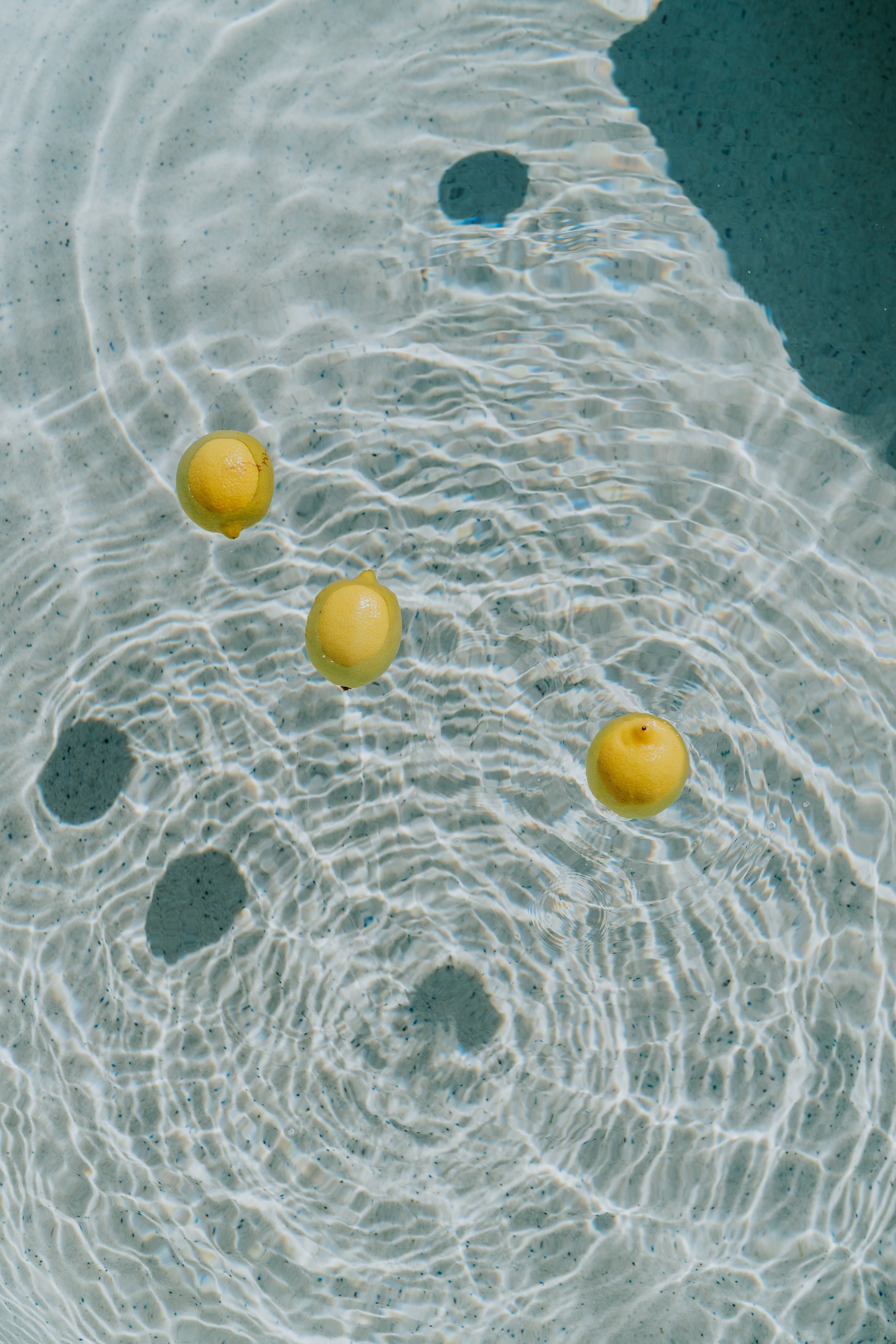 Three lemons floating in a clear water pool.