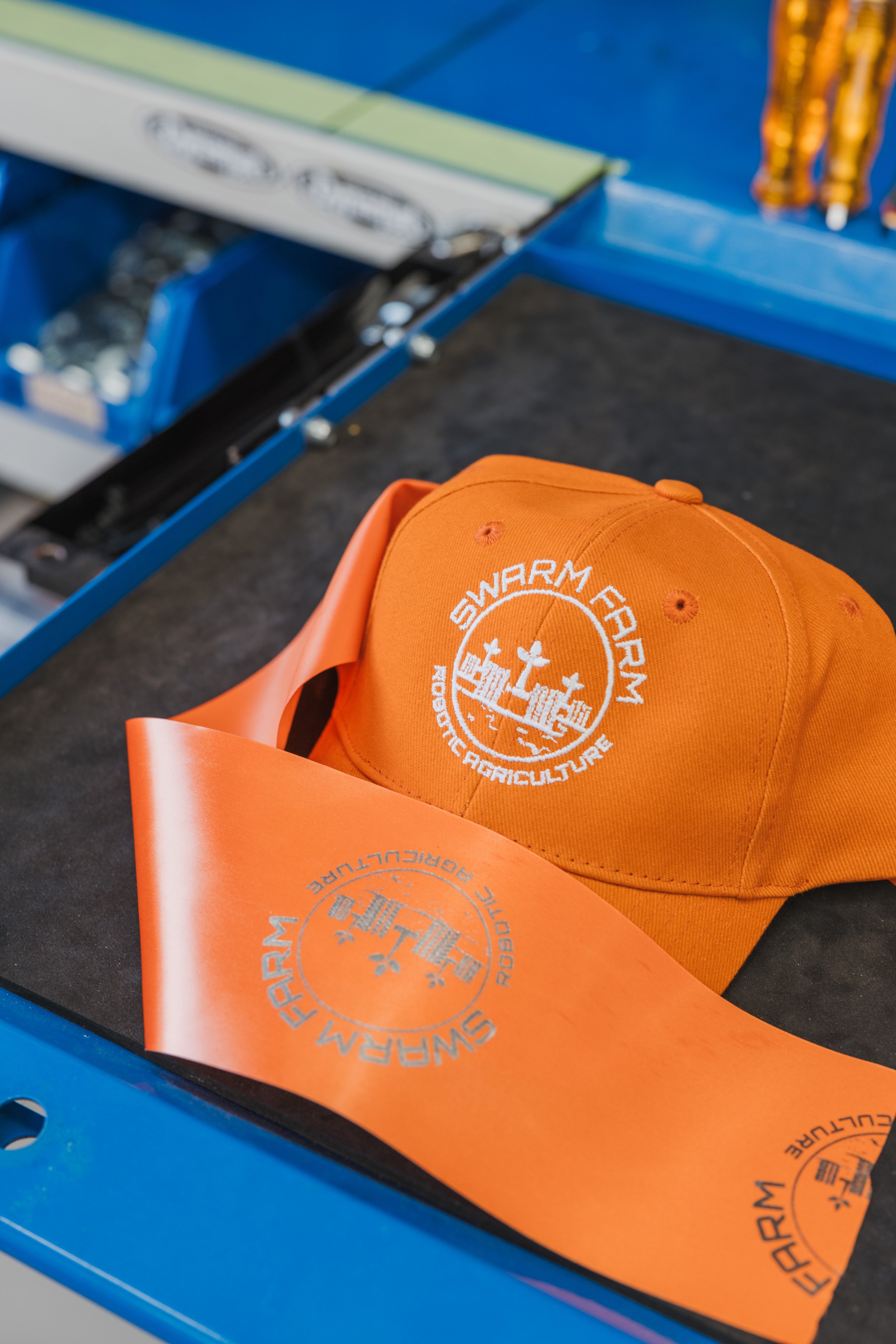 Orange hat with "Swarm Farm Robotic Agriculture" logo and design templates on a table.