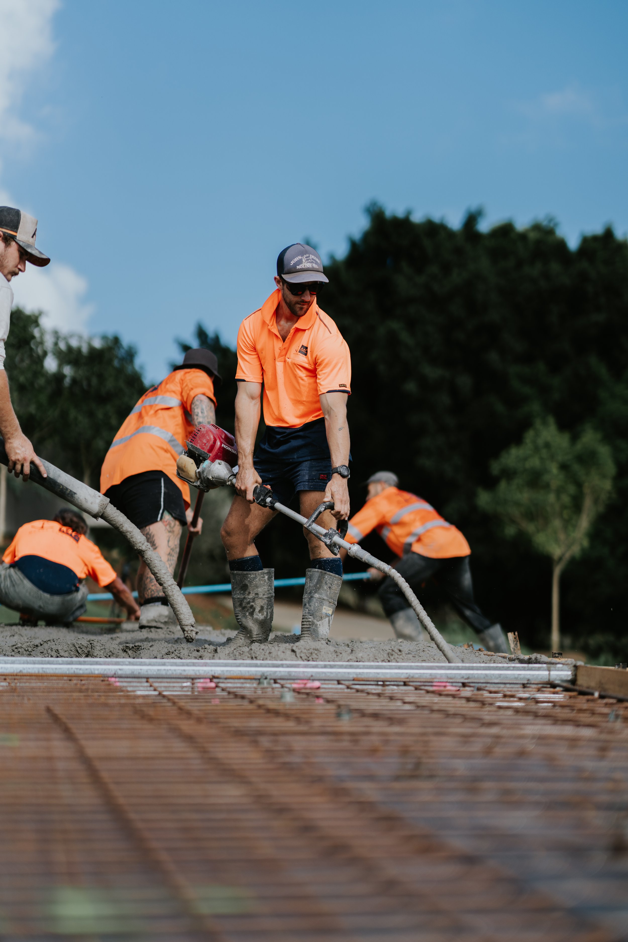 Construction workers in orange shirts pouring concrete on a construction site.