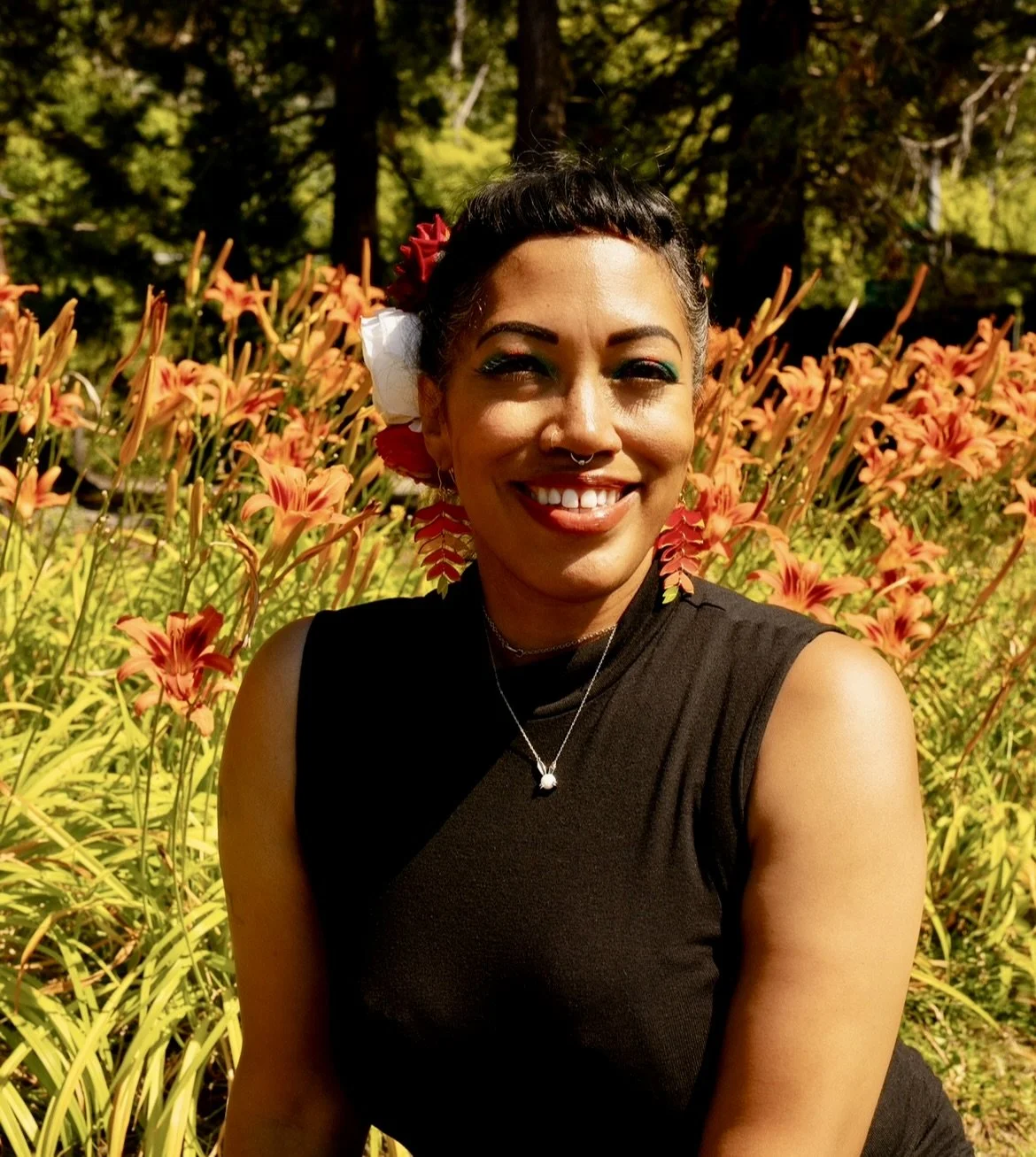 A woman smiling outdoors with vibrant orange and pink flowers behind her.
