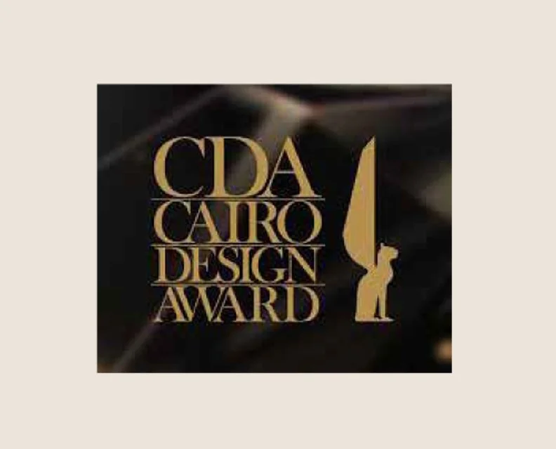 Logo of the Cairo Design Award, featuring a golden stylized writing quill and a person holding it, with the text 'CDA Cairo Design Award' in gold on a dark background.