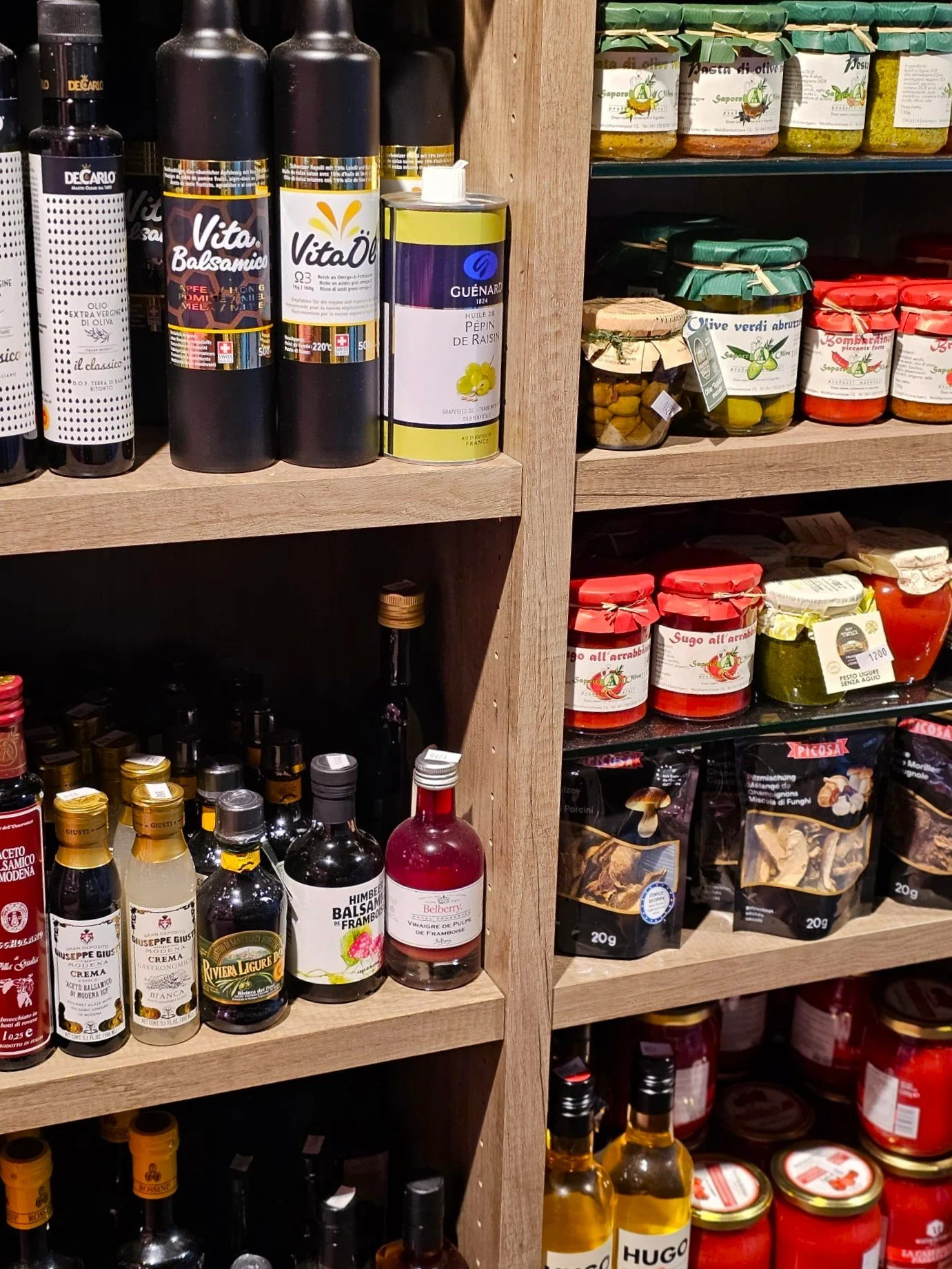 Regale mit verschiedenen italienischen Lebensmitteln, darunter Olivenöl, Pesto, Balsamico-Essig und eingelegte Oliven in Gläsern.