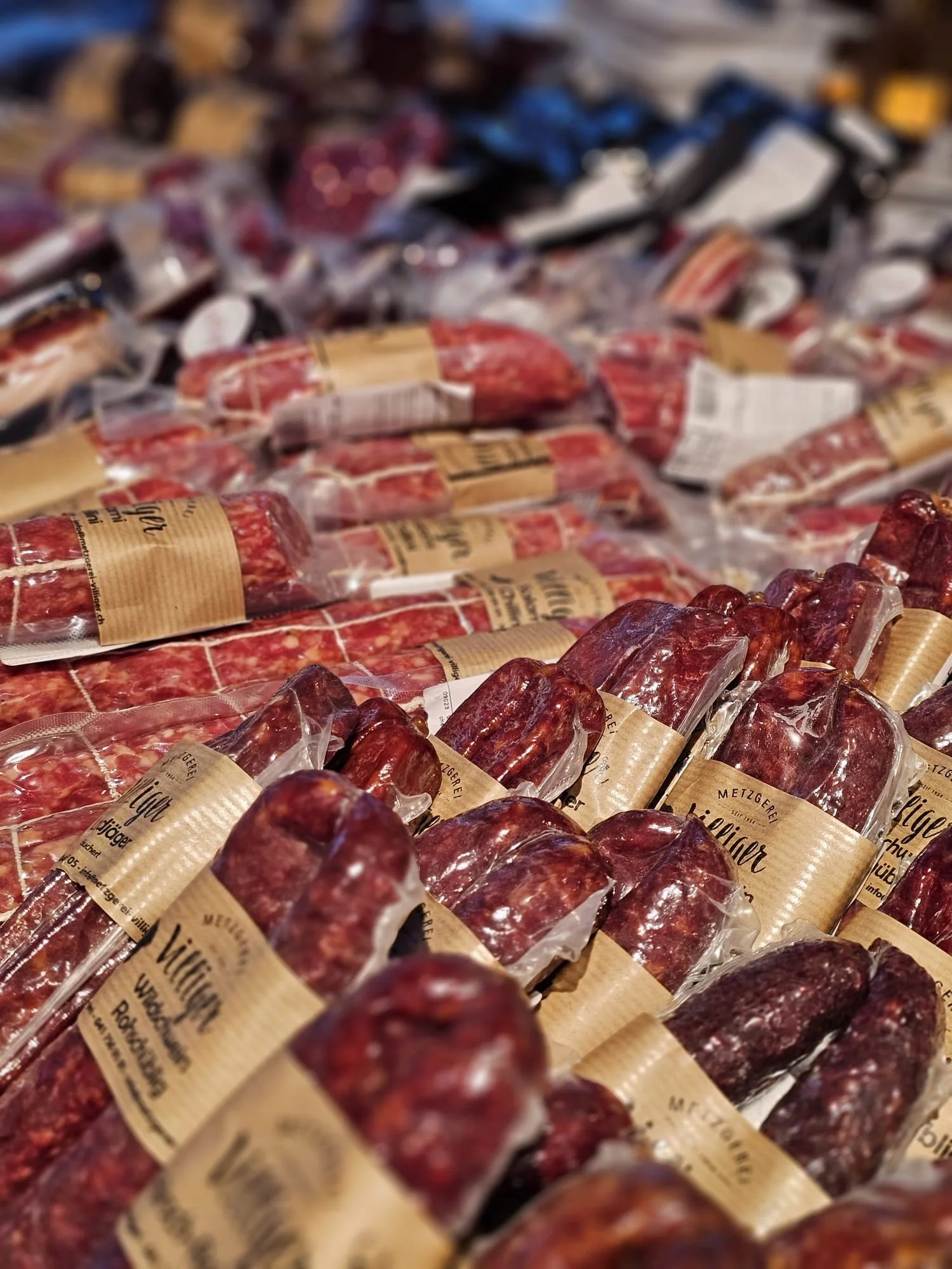 Mehrere Wurstpakete in einer Metzgerei, verpackt in transparente Plastikfolie mit braunem Etikett.