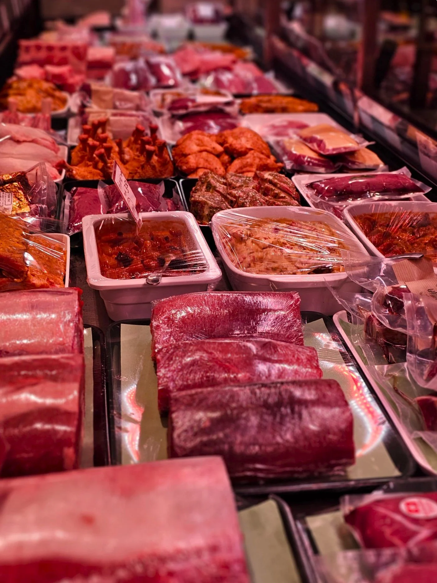 Verschiedene Fleischsorten und Fleischprodukte auf einem Metzger- oder Markttisch, verpackt in Plastikfolie oder in Behältern.