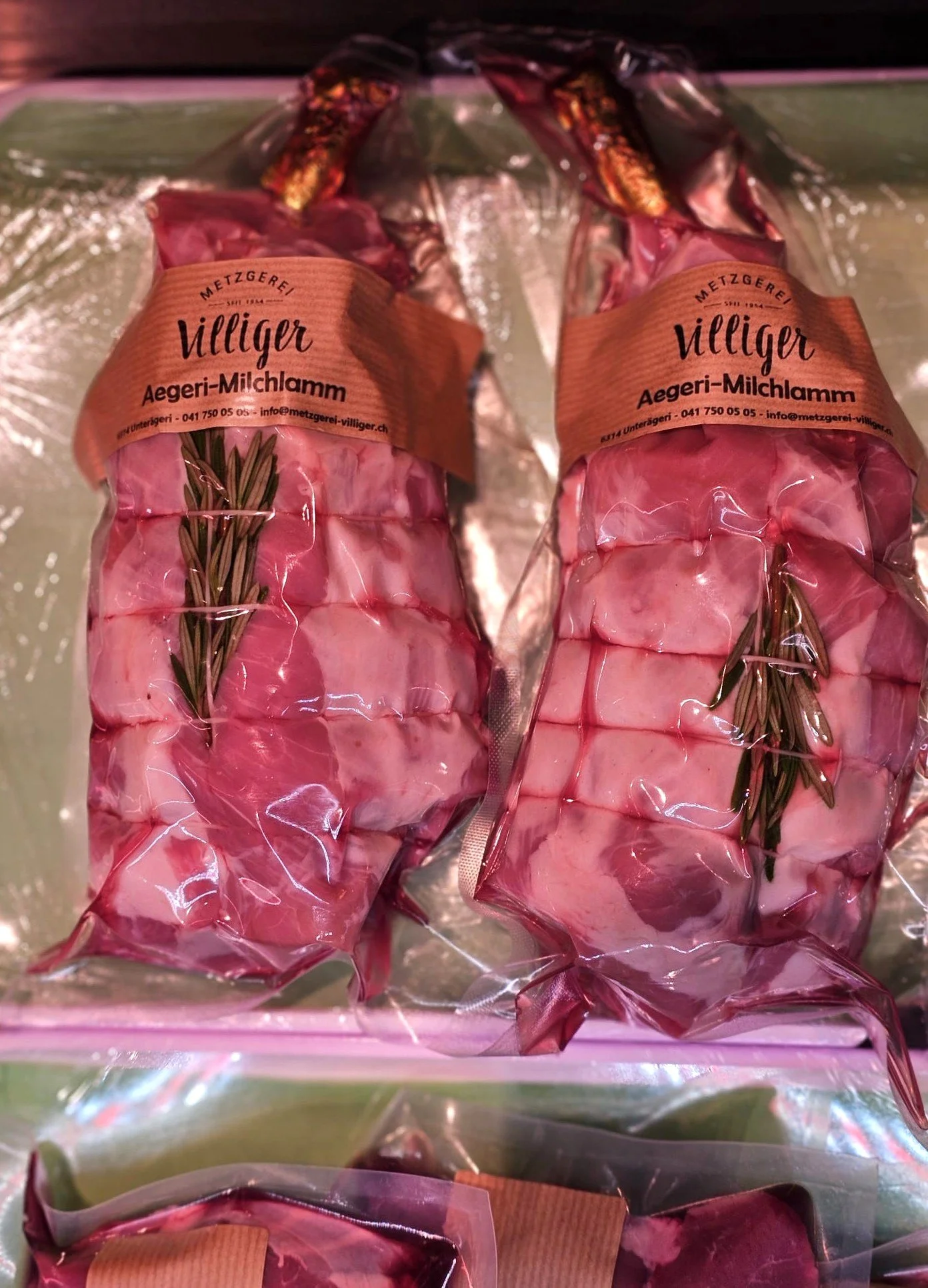 Zwei in vakuumverpackte Lämmerkeulen mit Rosmarin, etikettiert mit "Villiger Aegeri-Milchlamm" von Metzgerei Villiger.