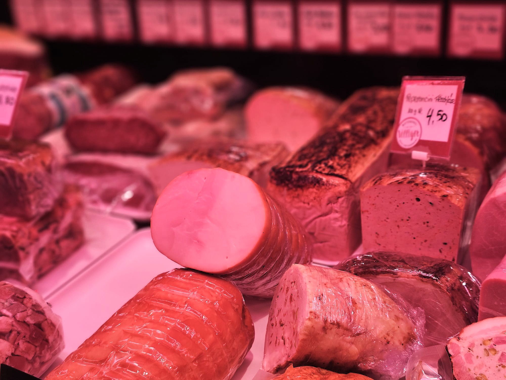 Verschiedene Fleischstücke im Supermarkt, einige sind geräuchert und gewürzt, andere sind roh, mit pinken Preisschildern daneben.