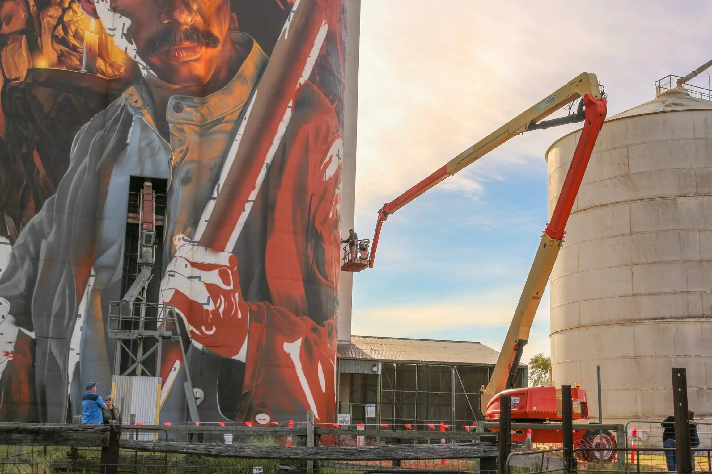 a picutre of an artist in a large boom lift using spray cans to paint a giant silo artwork 