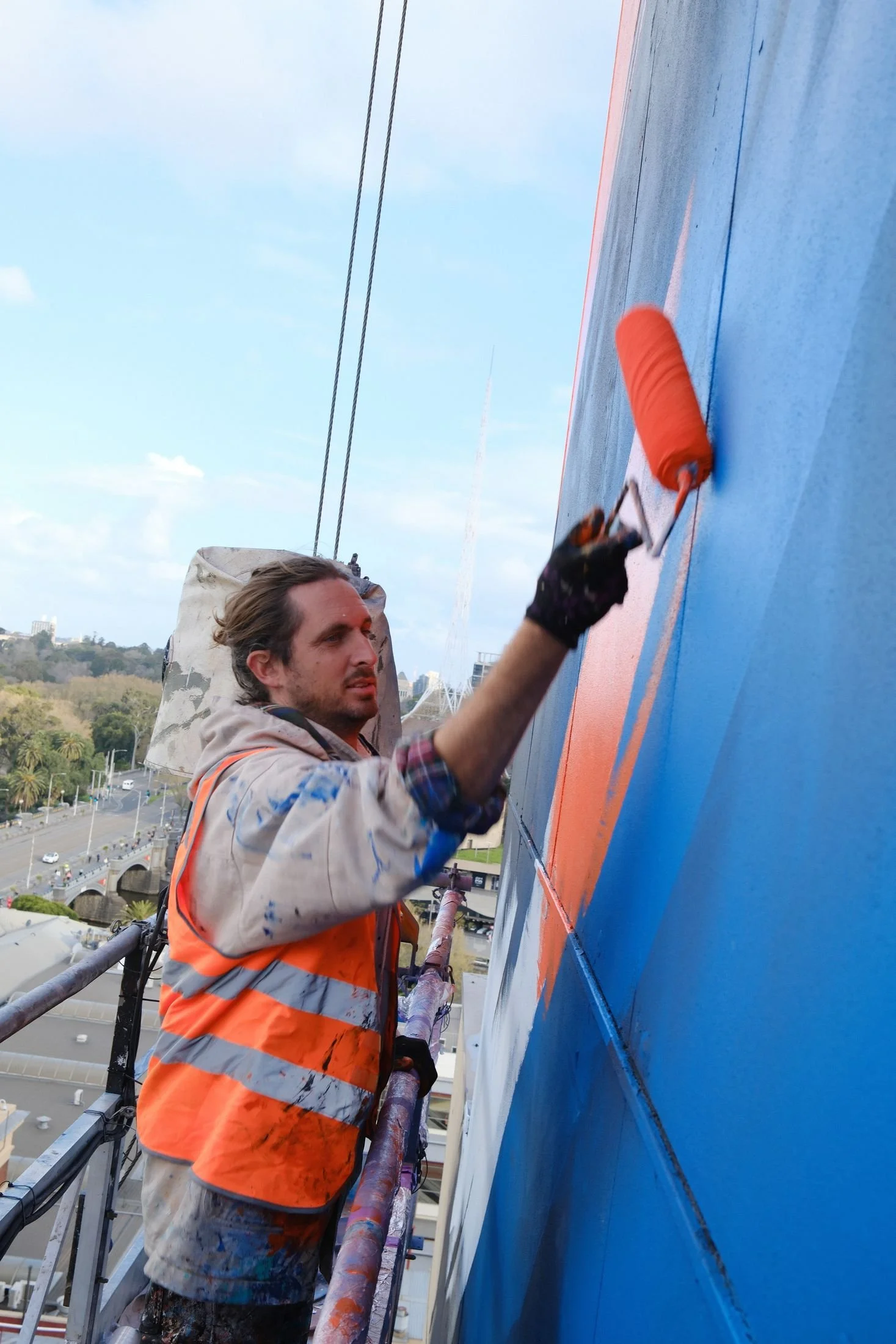 Adnate rolling orange paint on the swing stage