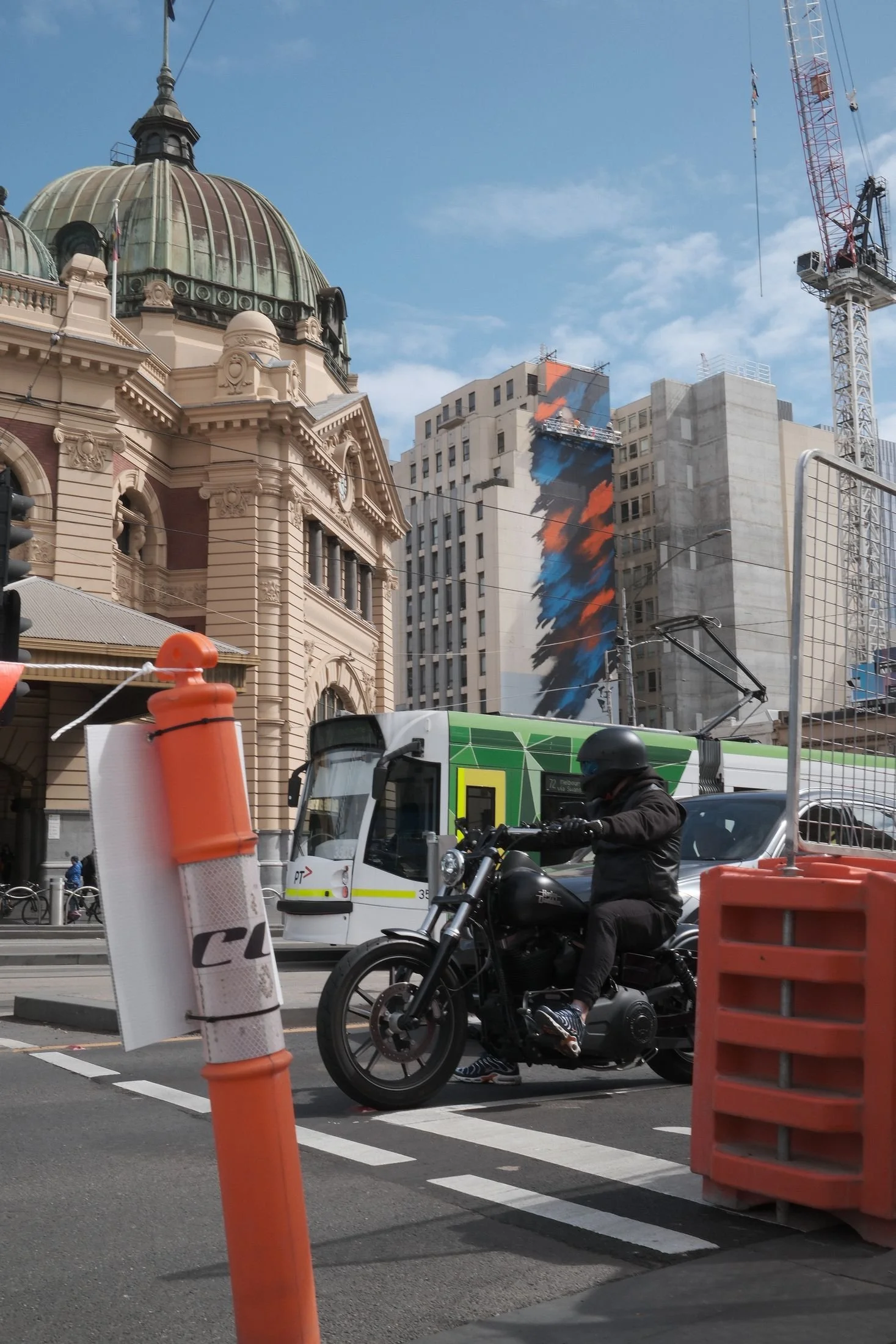 The mural in progress above Flinders Street, with a tram and traffic below