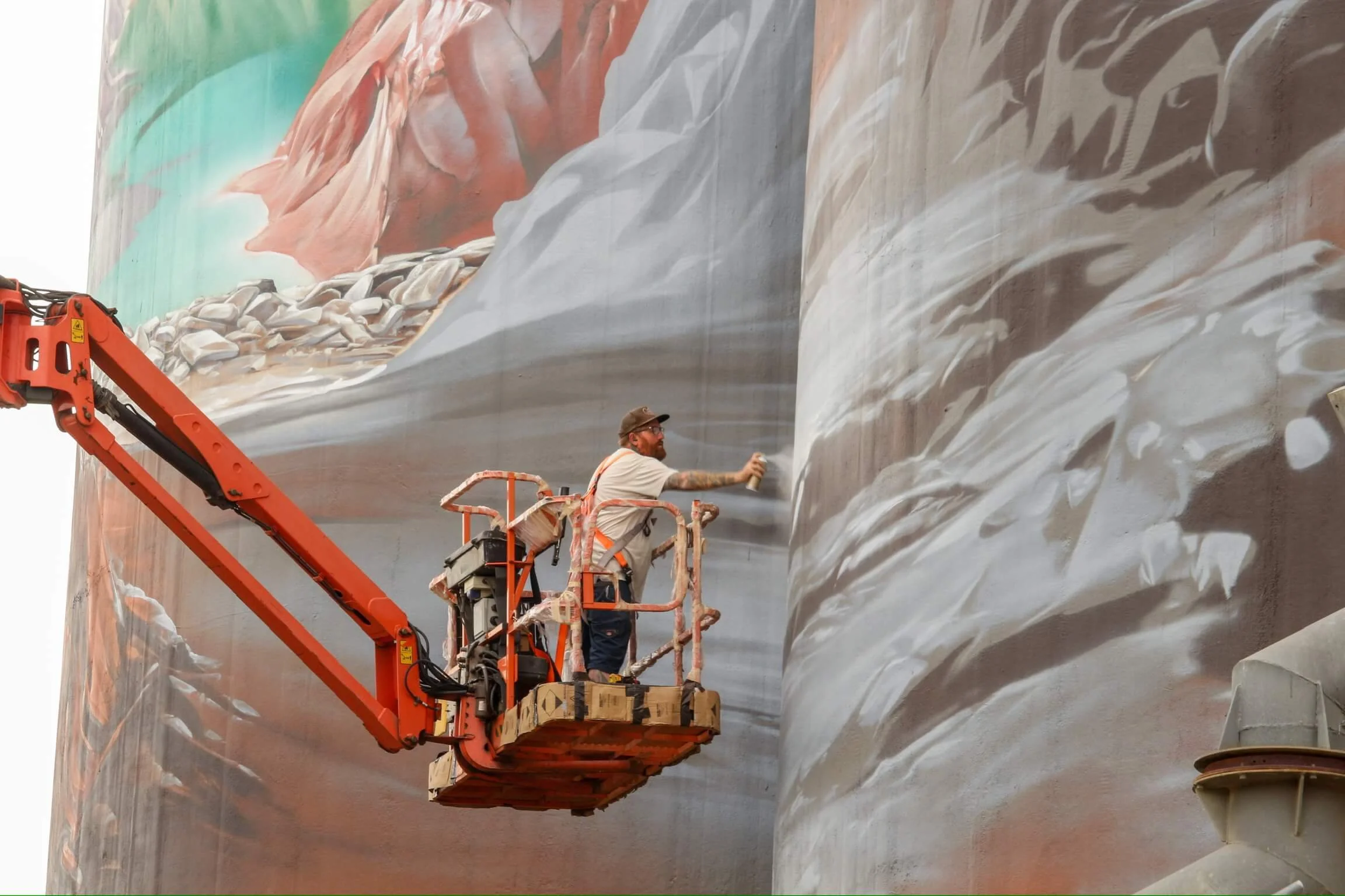 image of an artist using spray cans to paint a large silo art work 