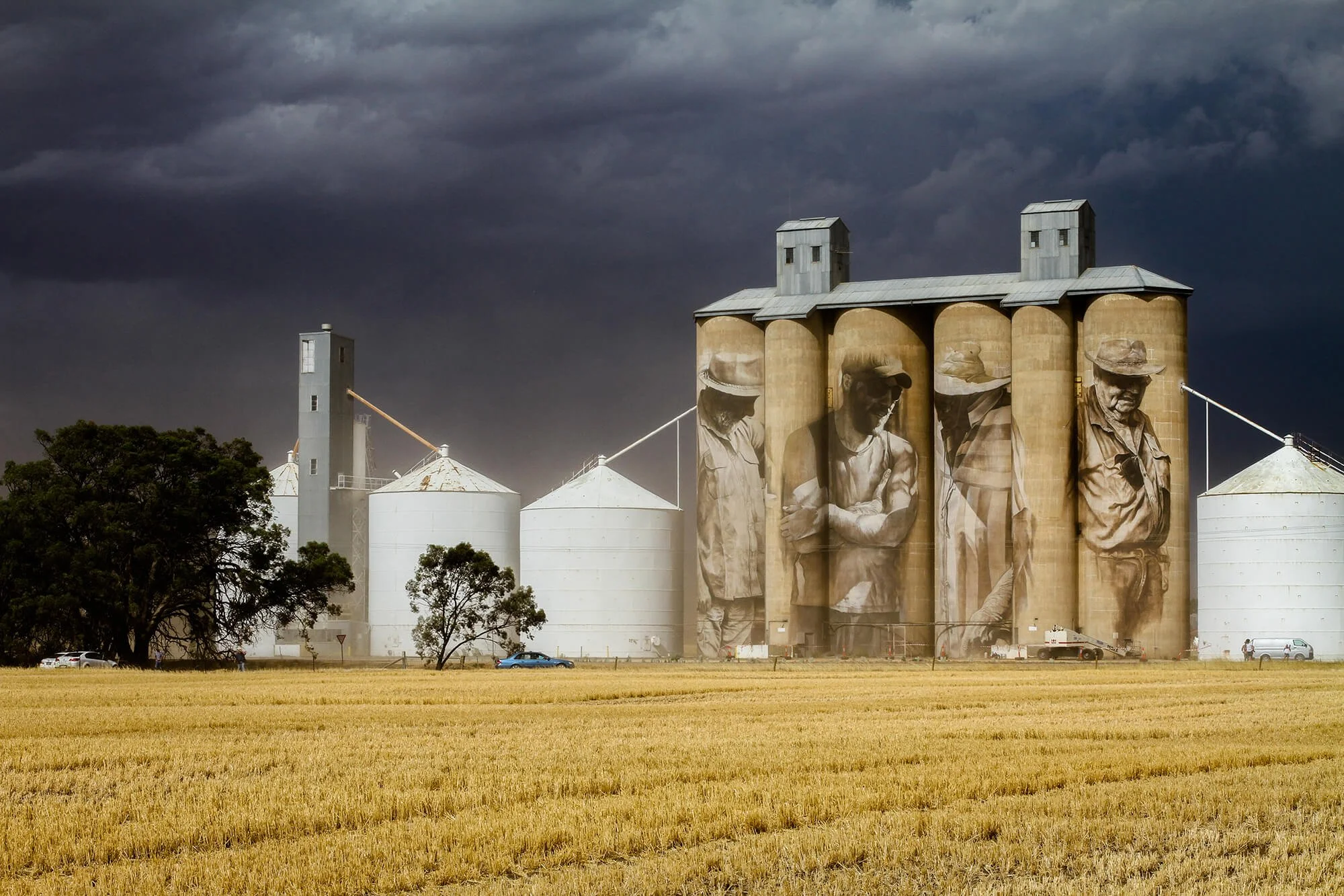 an image of a silo artwork on giant grain silo with dark and stomry couds making the mural art look bright and high contract