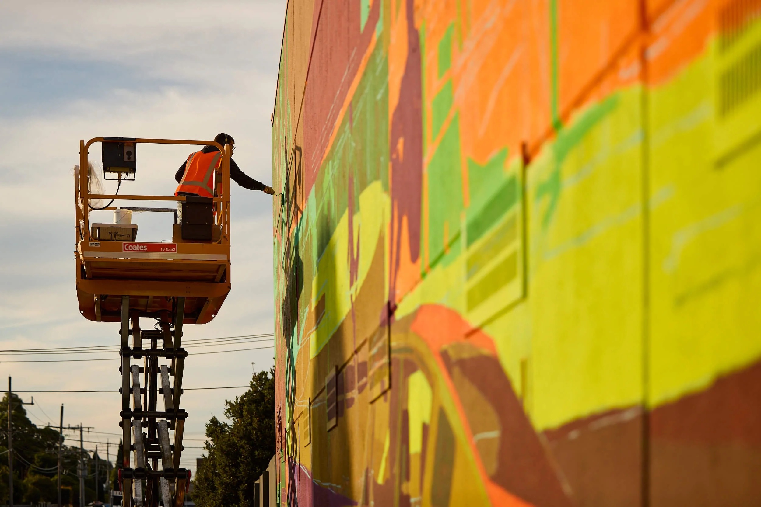 an artist on a lift paints a giant street art mural