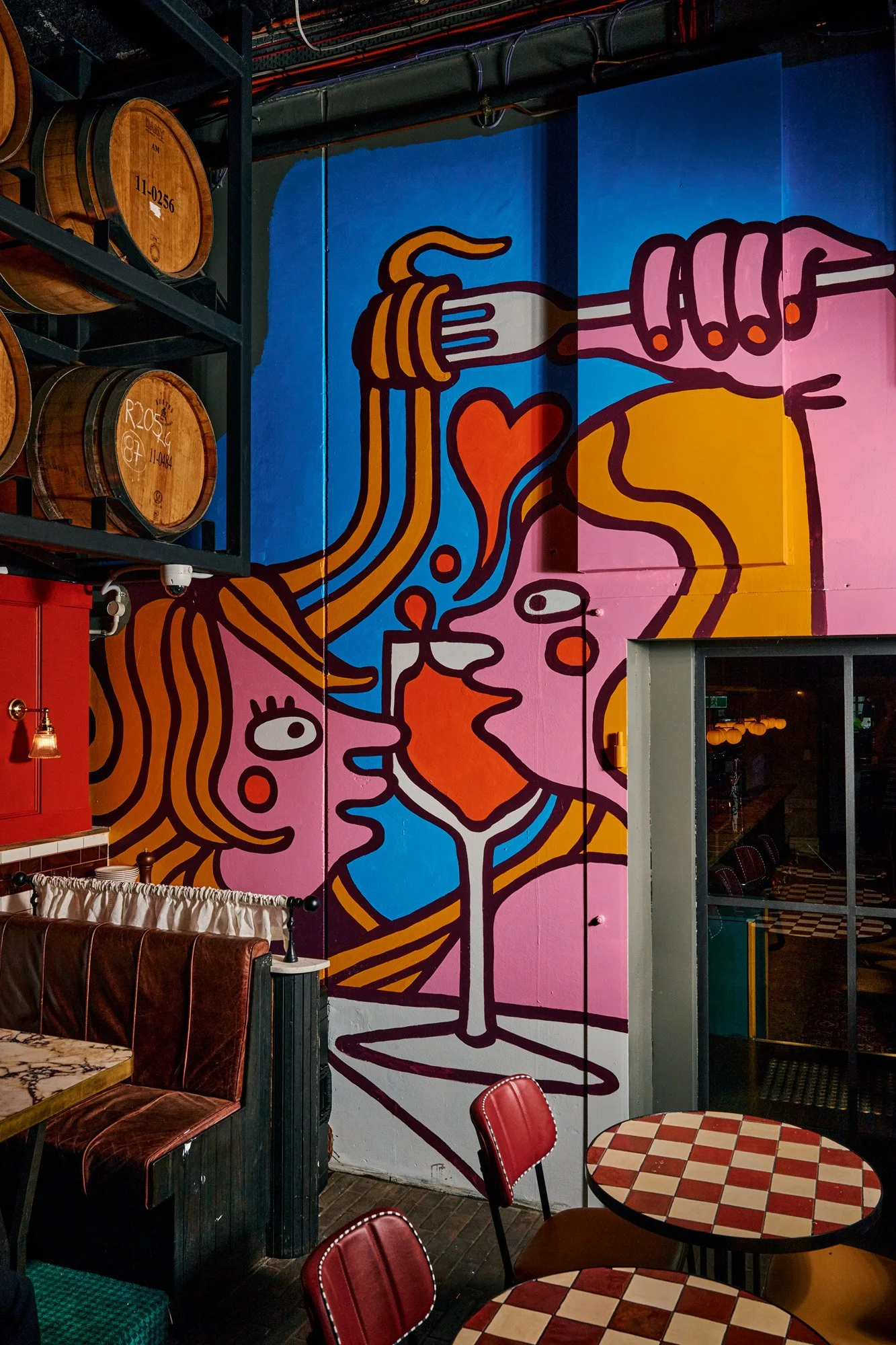 Colorful mural featuring abstract faces and hands, with a fork and knife, in a restaurant or cafe setting.