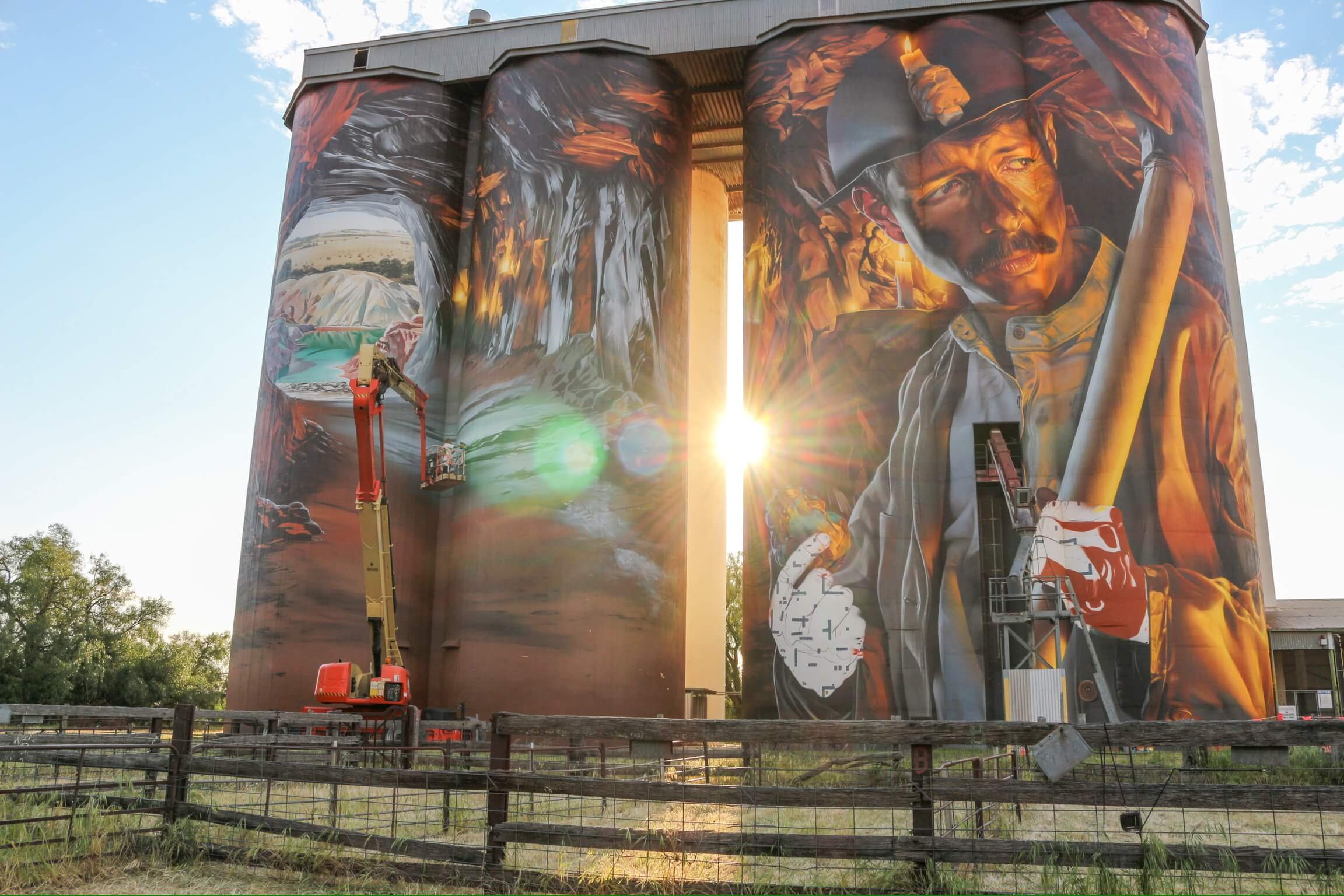 a picture of silo art in kapunda of a miner holding copper with the sun setting in the background