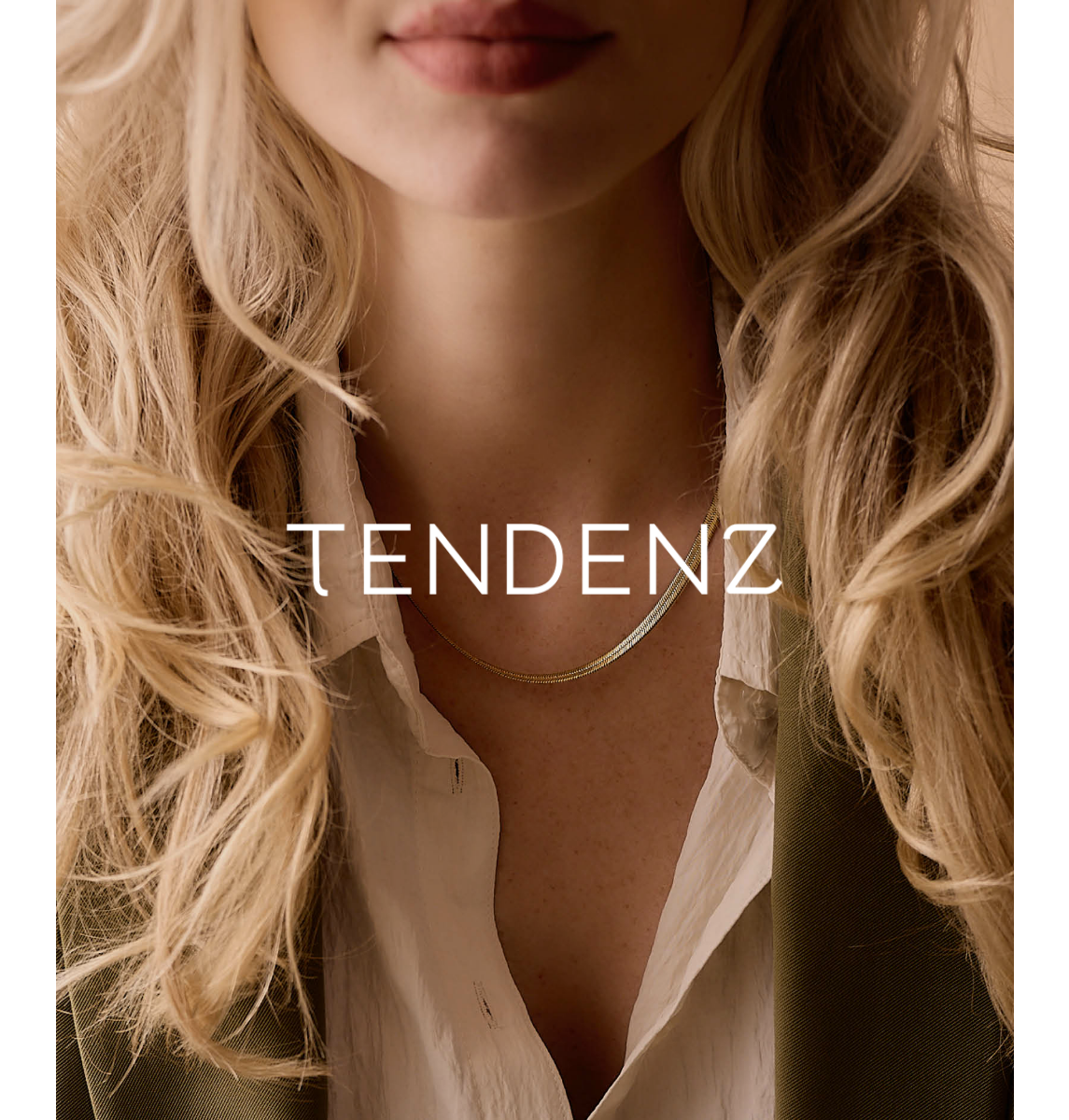 Nærbilde av en kvinnes hake, lepper og del av overkroppen, med blondt, krøllet hår, hvit skjorte og gullkjede, med teksten "TENDENZ" på bilde.