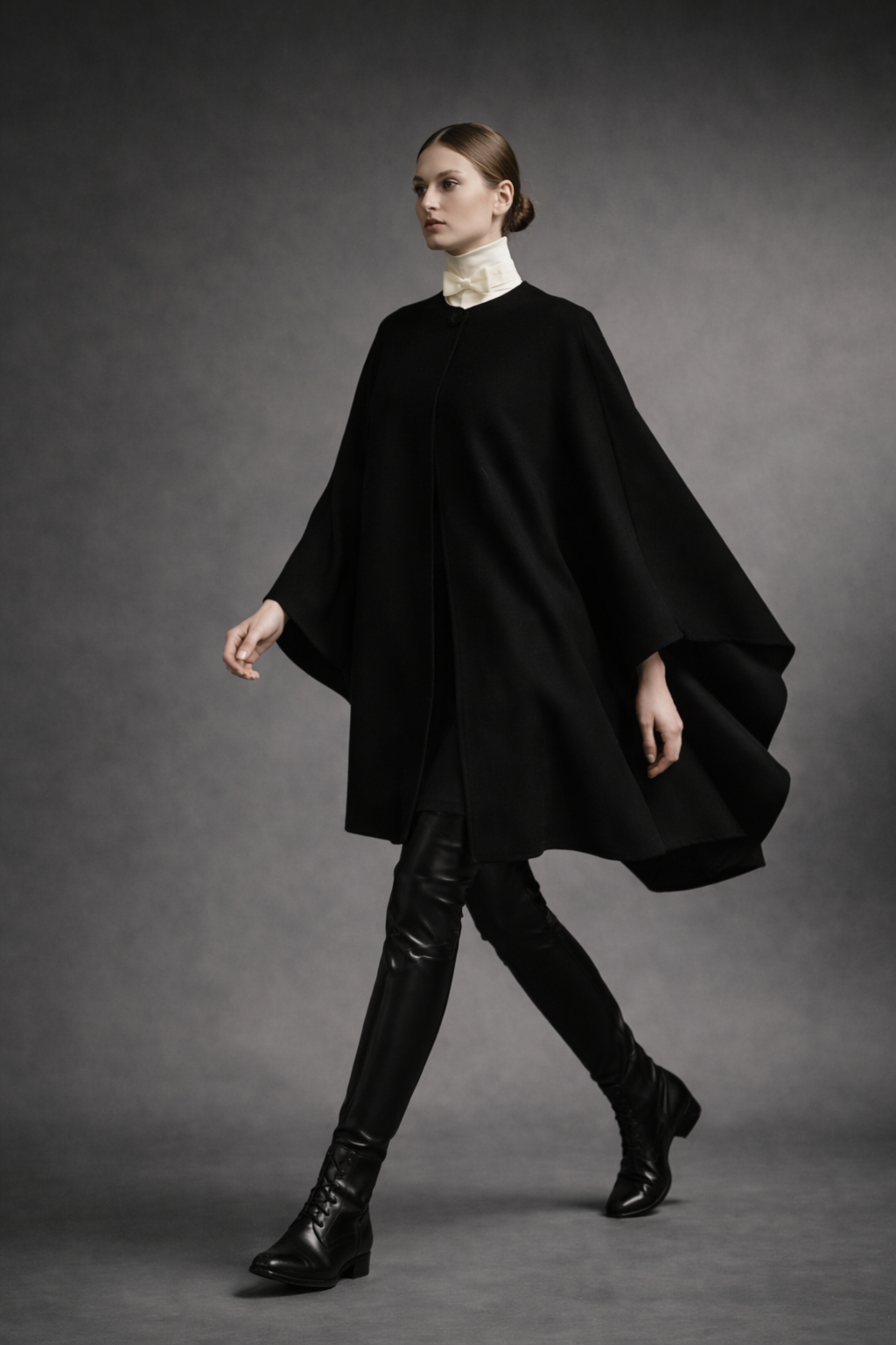 Audrey house icon cape in black double-faced cashmere, with rounded neckline and signature button, styled with off-white collar and bow.