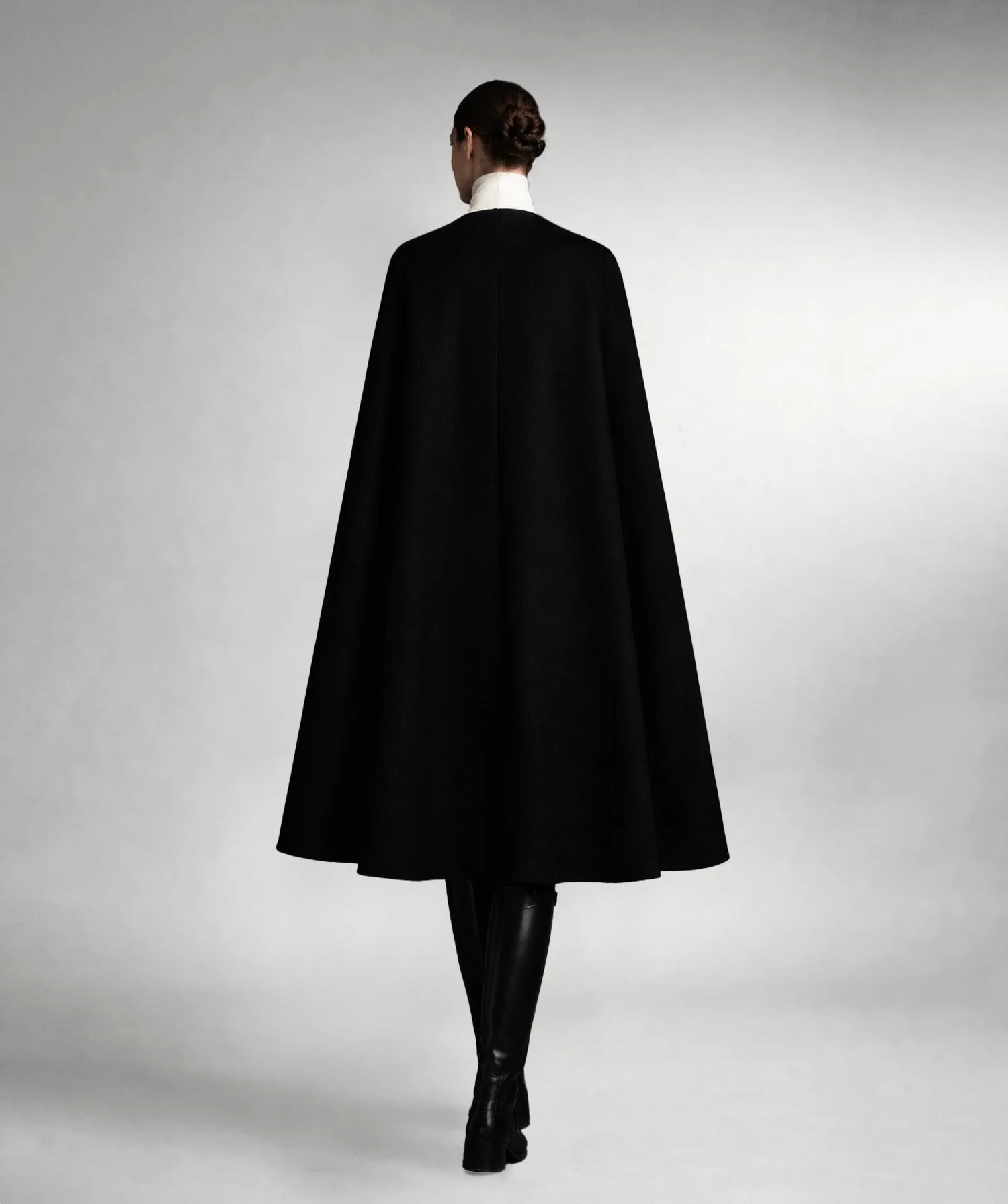 Black cape on model in motion with flowing shape, photographed in low light for a minimalist fashion portrait