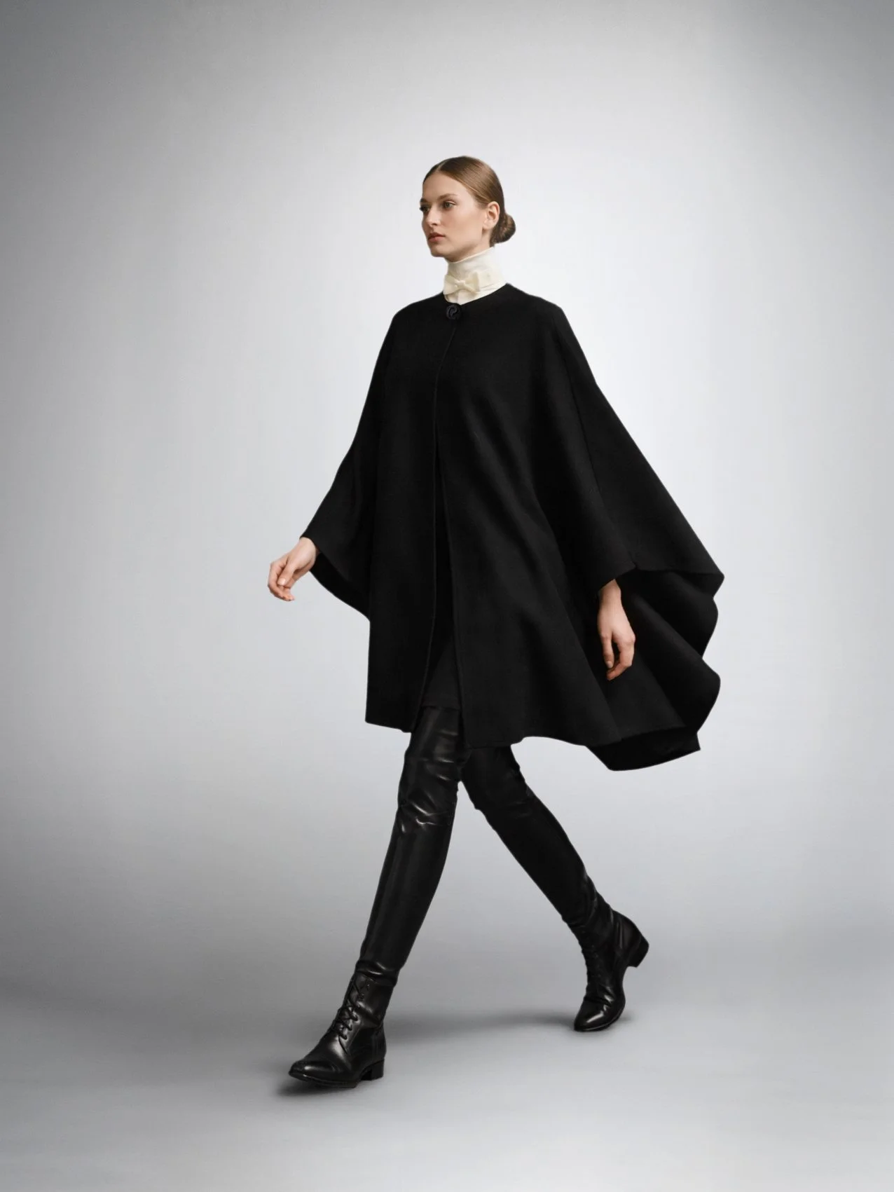 Model in motion wearing the CASTELLAINES black cape with flowy silhouette and signature button closure