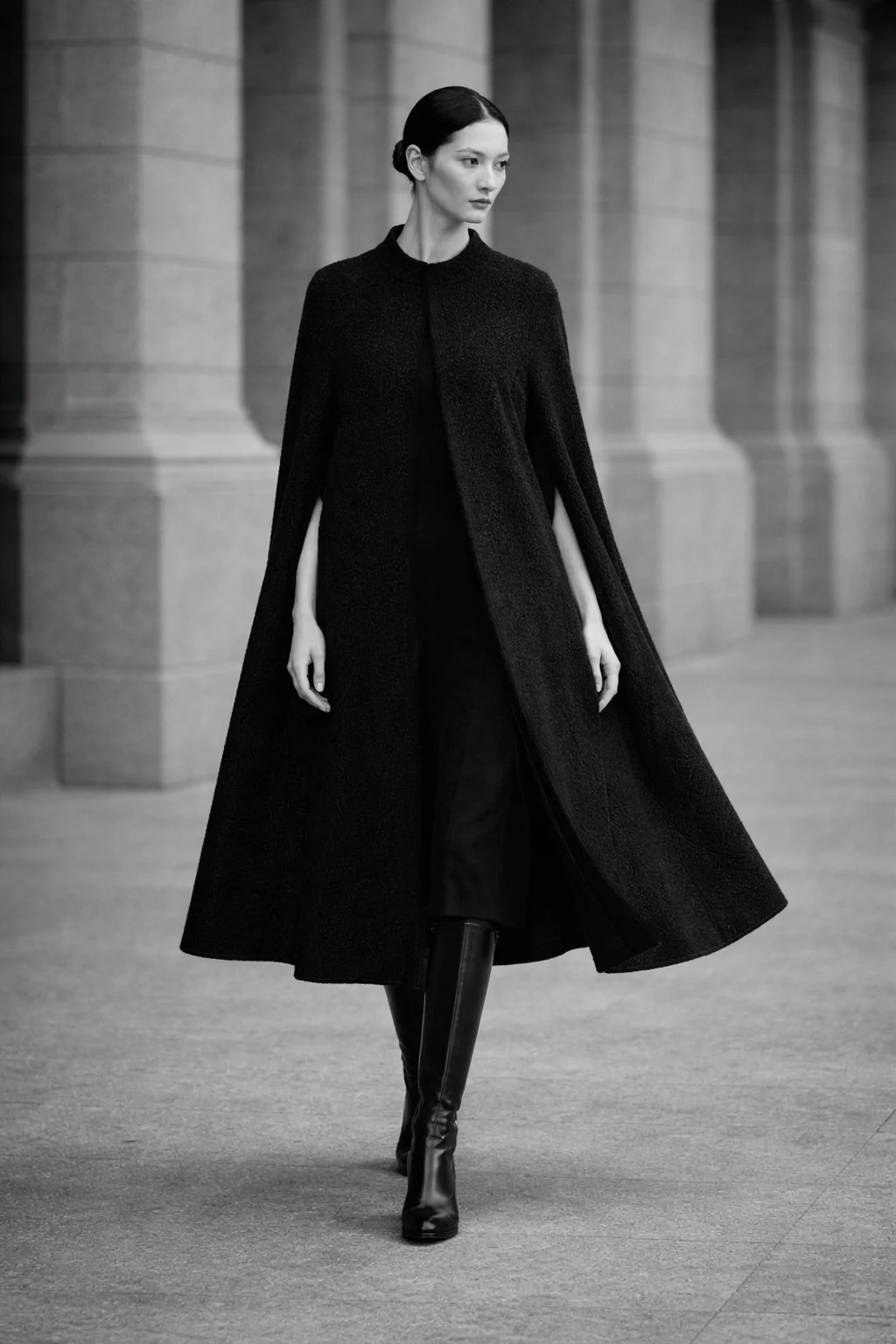 Model wearing the CASTELLAINES black cape, highlighting the A-line silhouette, round neckline, and architectural drape.
