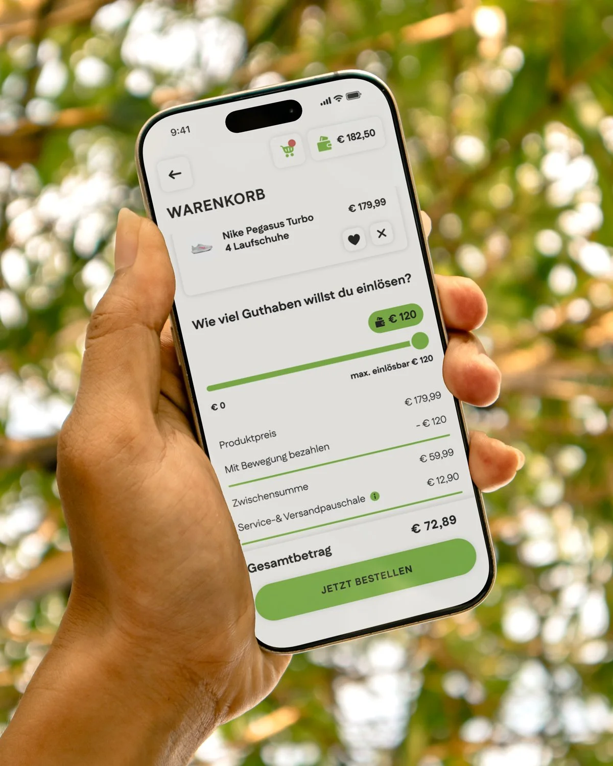 Hand hält ein Smartphone mit der Move to Pay-App, zeigt einen Warenkorb mit Nike Pegasus Turbo Laufschuhe und einem Zahlungsbetrag von 72,89 Euro, mit einem Hintergrund aus grünen Blättern.