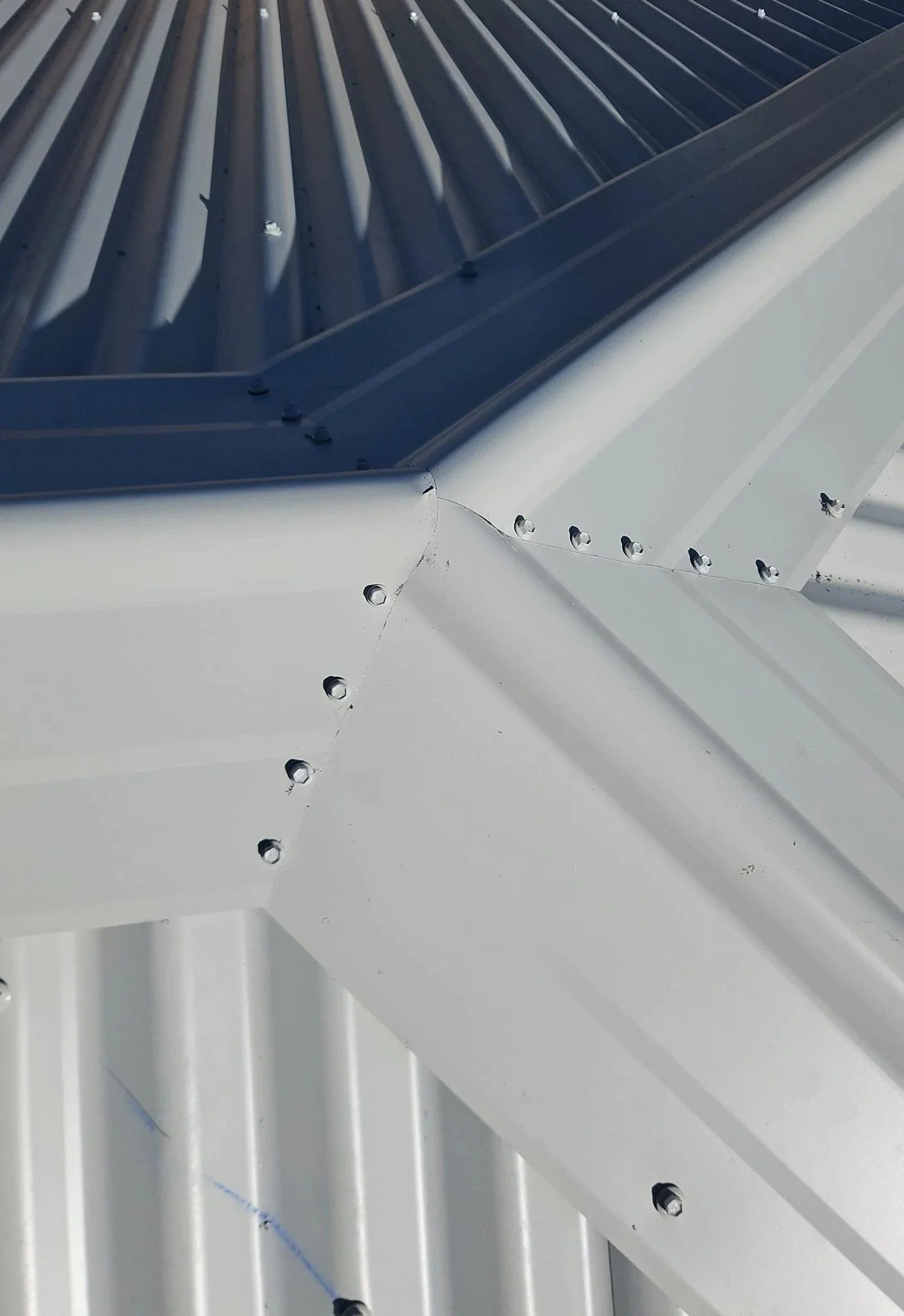 Close-up of a metal roof corner, showing white and blue painted corrugated metal panels fastened with screws.